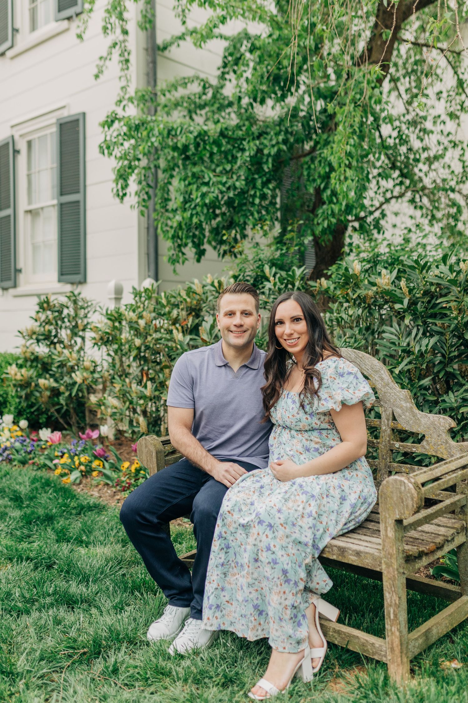 A couple sits together on a wooden bench in a lush garden setting.