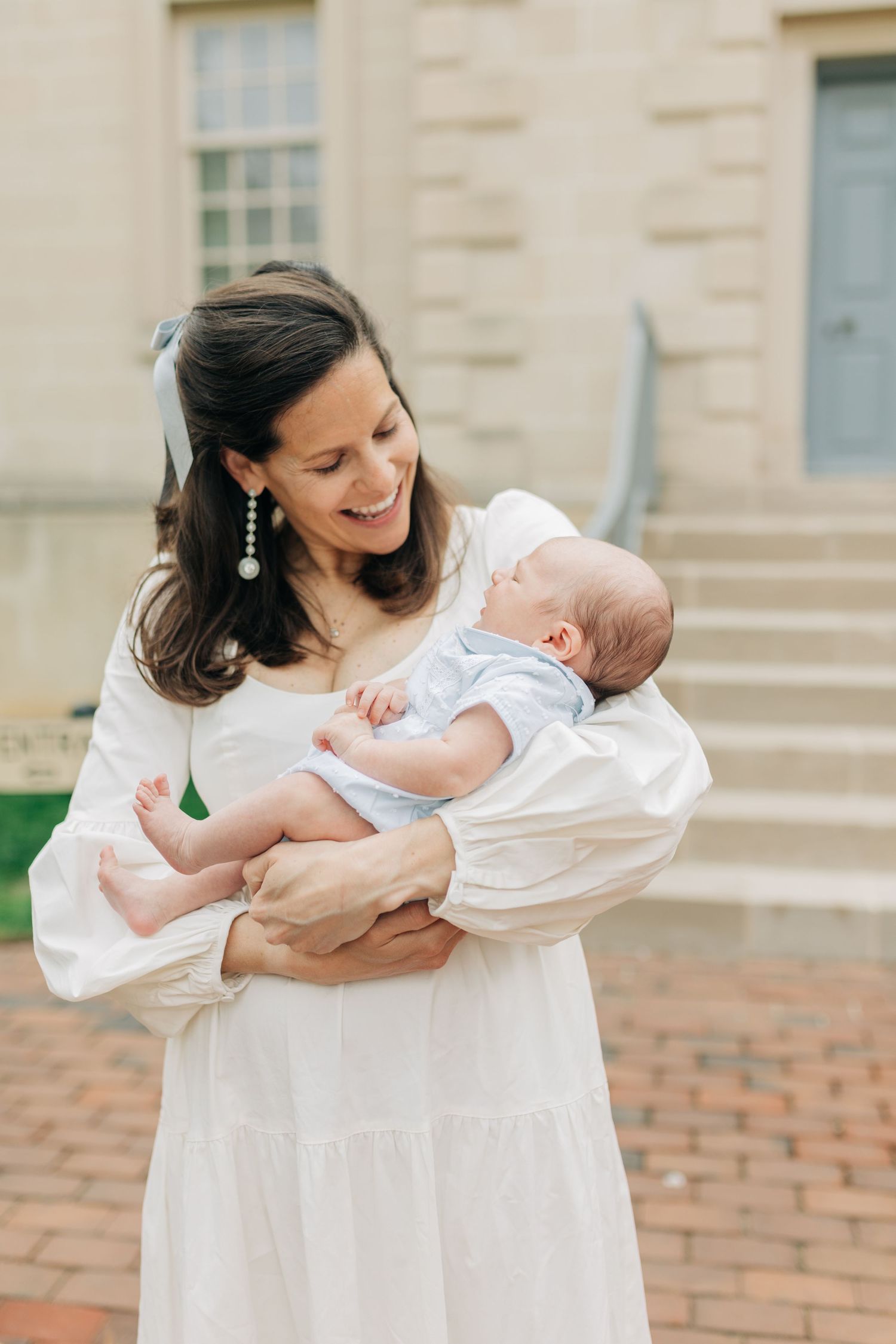 A tender moment between parent and infant in white clothing on brick steps.