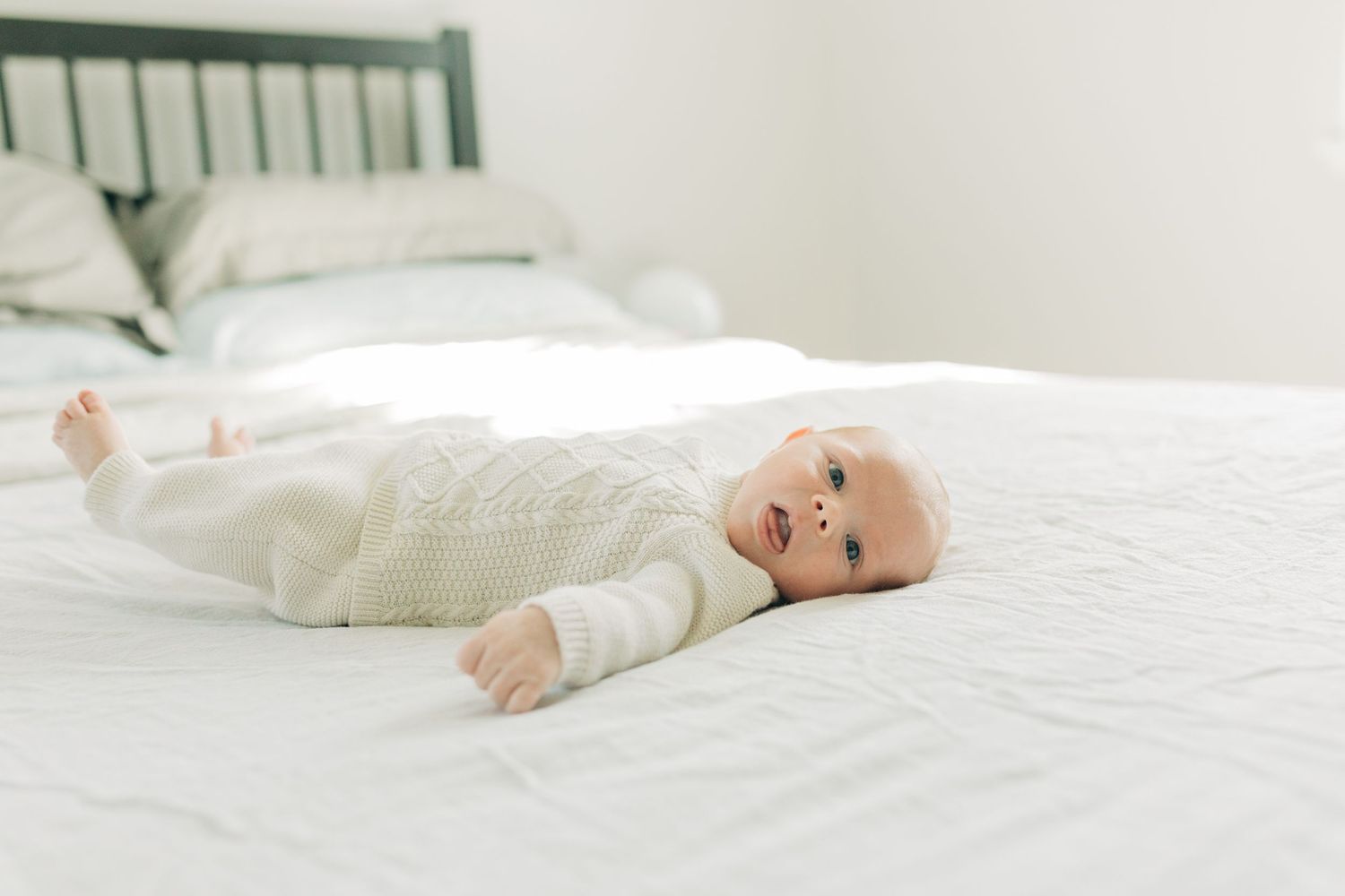 Infant lying on white bed with green headboard in background.