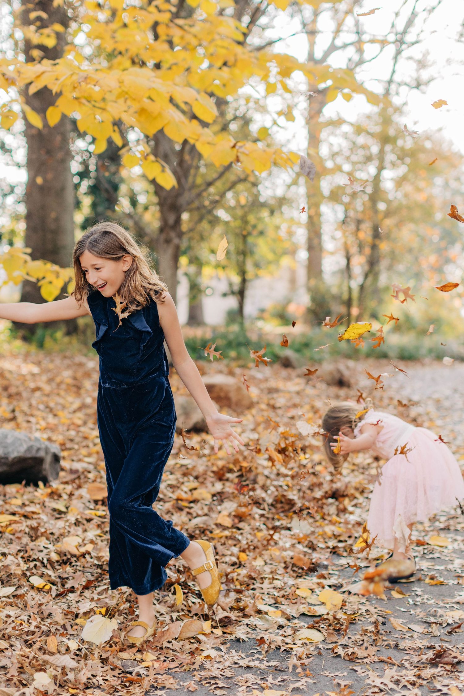 A playful scene of someone tossing autumn leaves in the air while wearing a navy dress.
