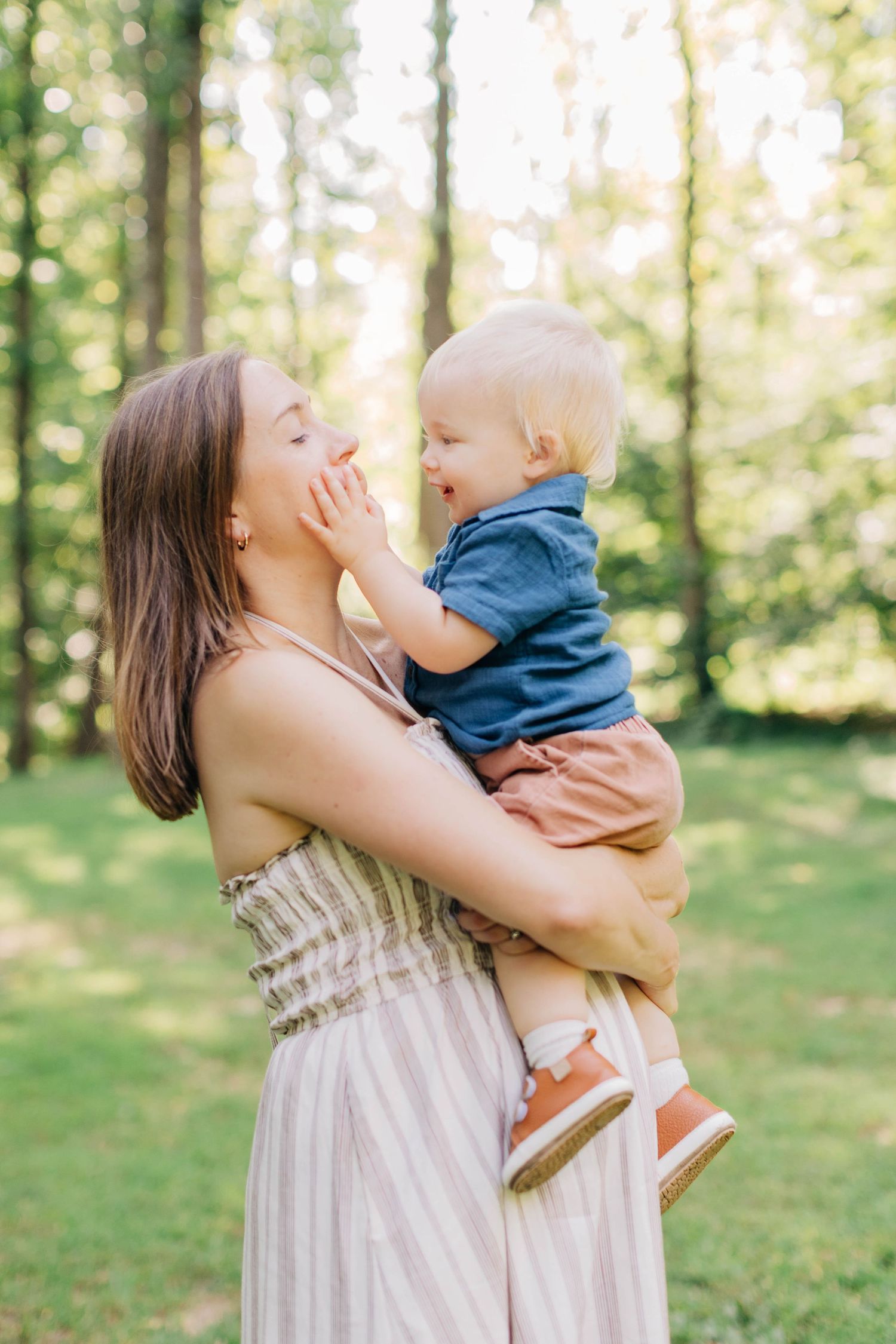 Mother holding laughing baby outdoors in a sunny green park setting.