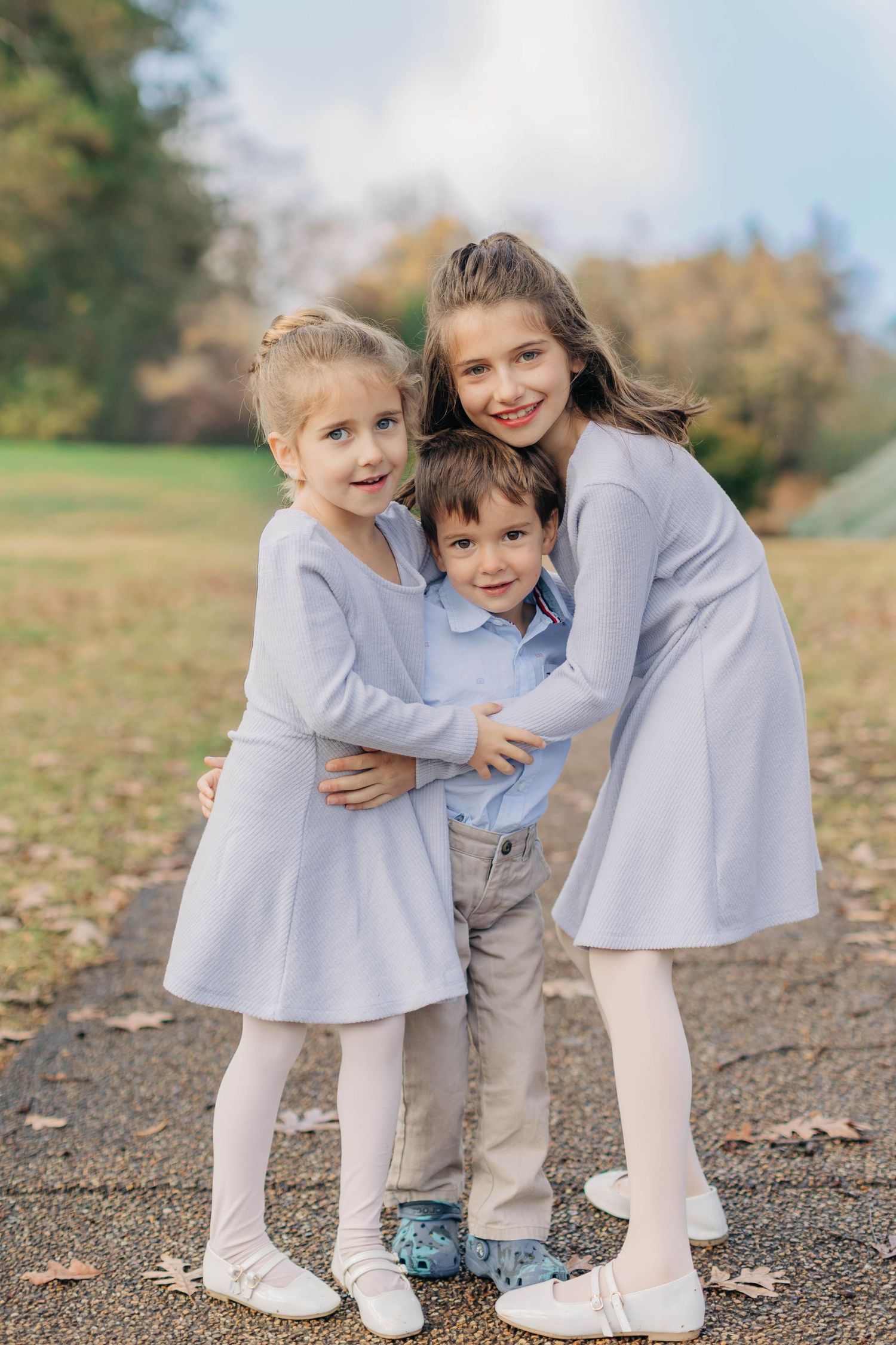 Three children in coordinating outfits share a joyful embrace outdoors.