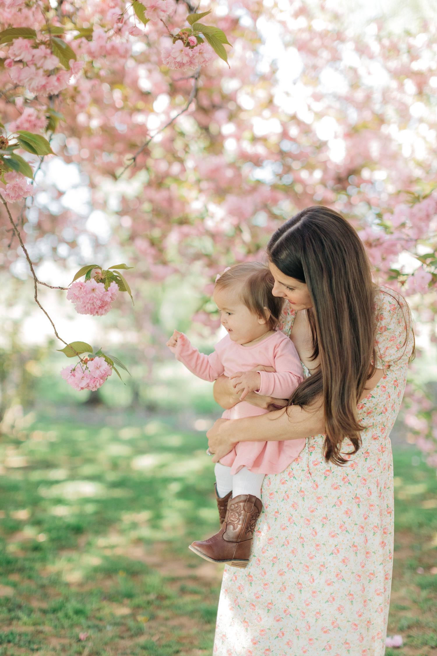 People in floral dresses enjoy spring blossoms under pink flowering cherry trees.