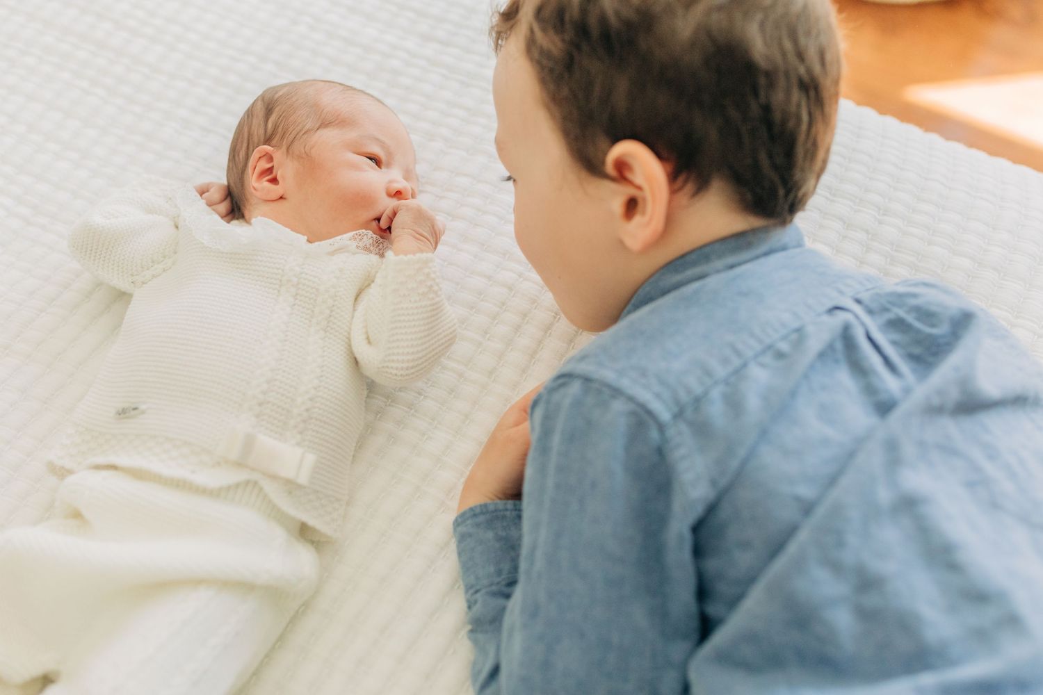 Sweet interaction between children on white bedding in natural light.