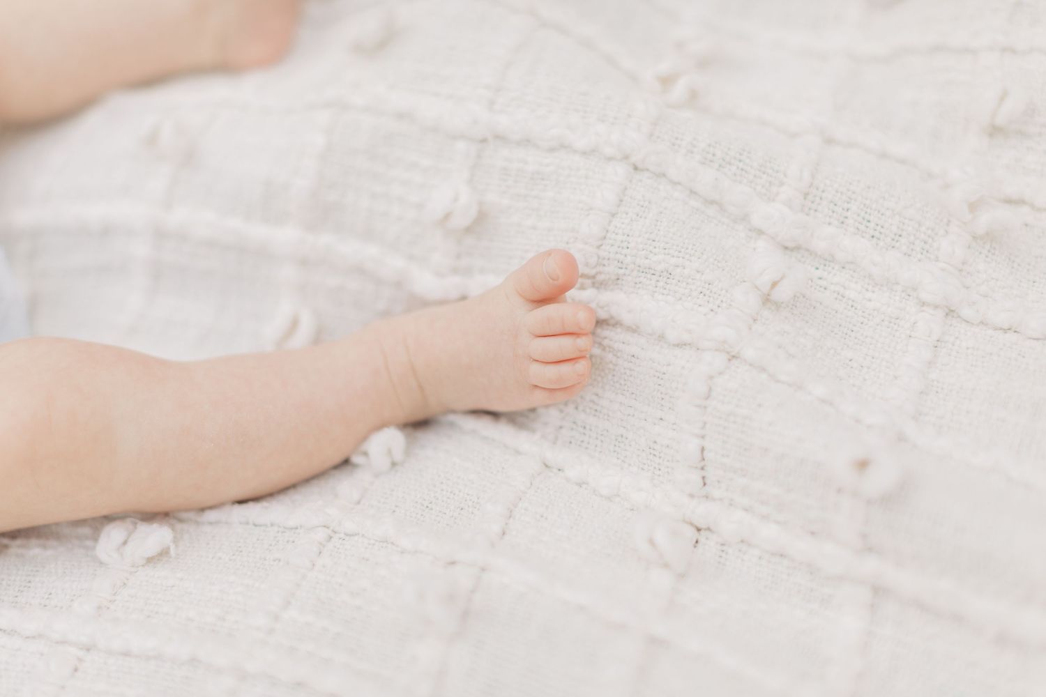 Close-up of a tiny baby hand resting on white textured fabric.