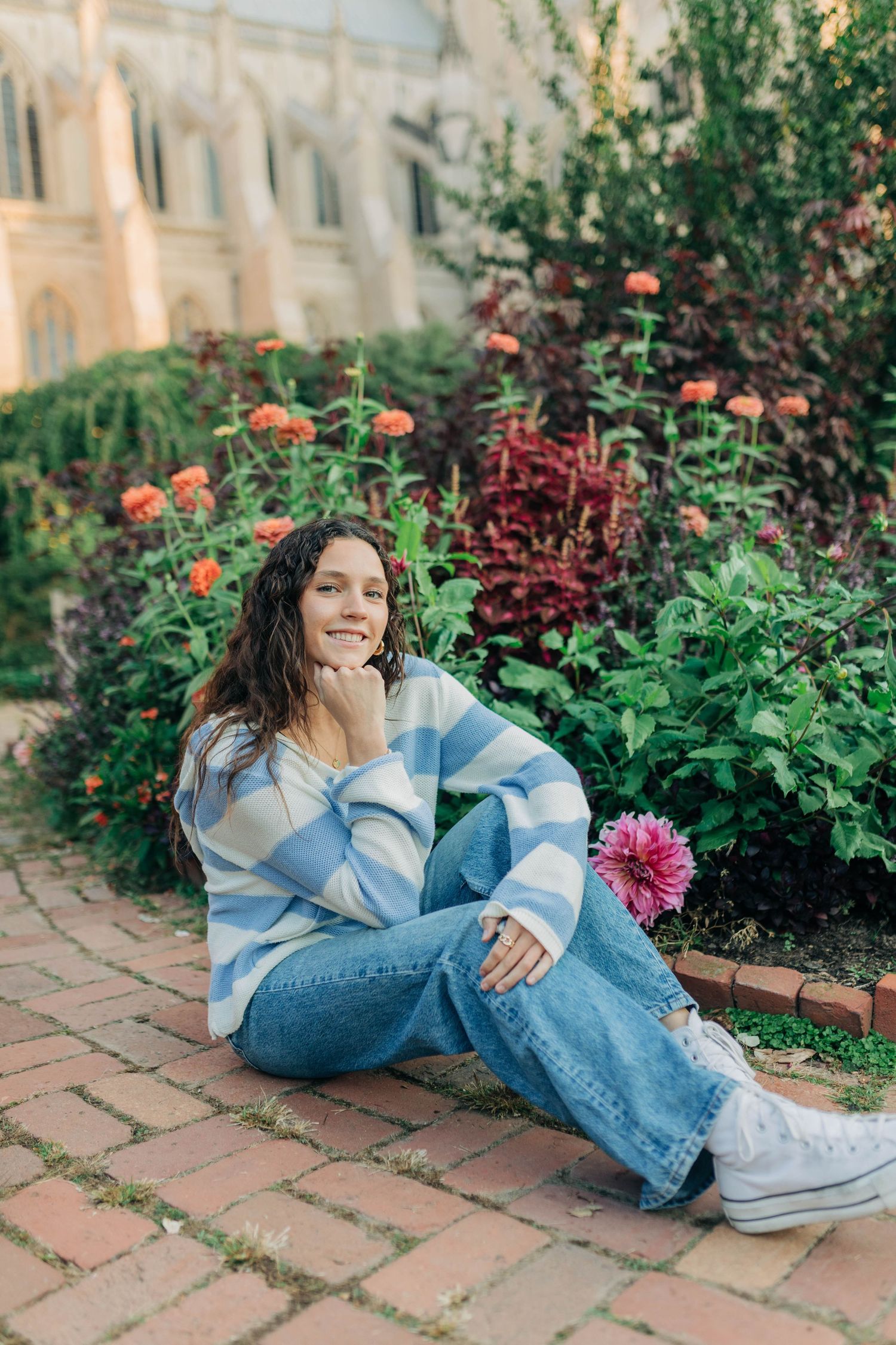 A casual portrait of someone relaxing on brick pavers surrounded by blooming flowers.
