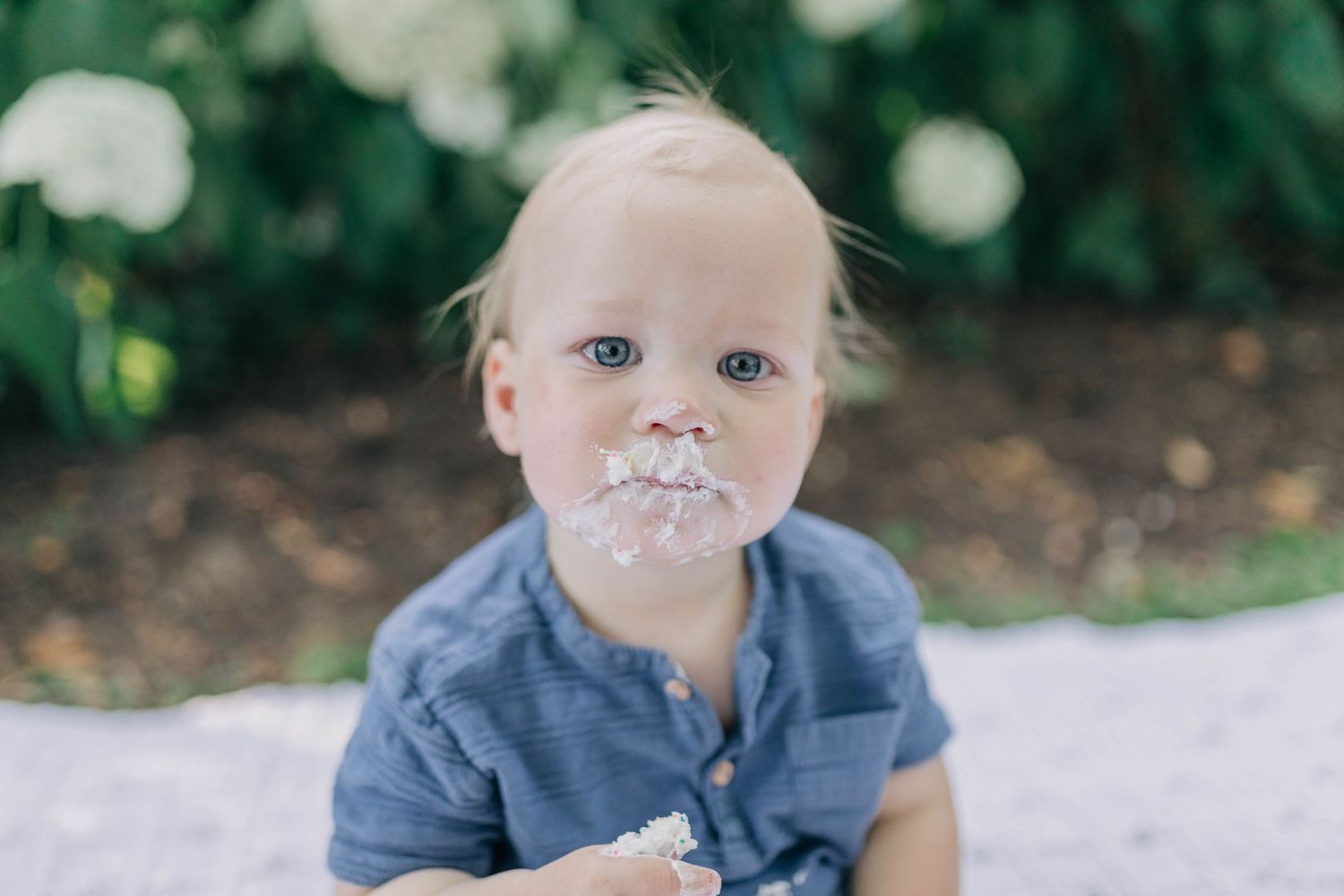 Close-up portraits of baby in blue outfit with sweet expressions against garden background.