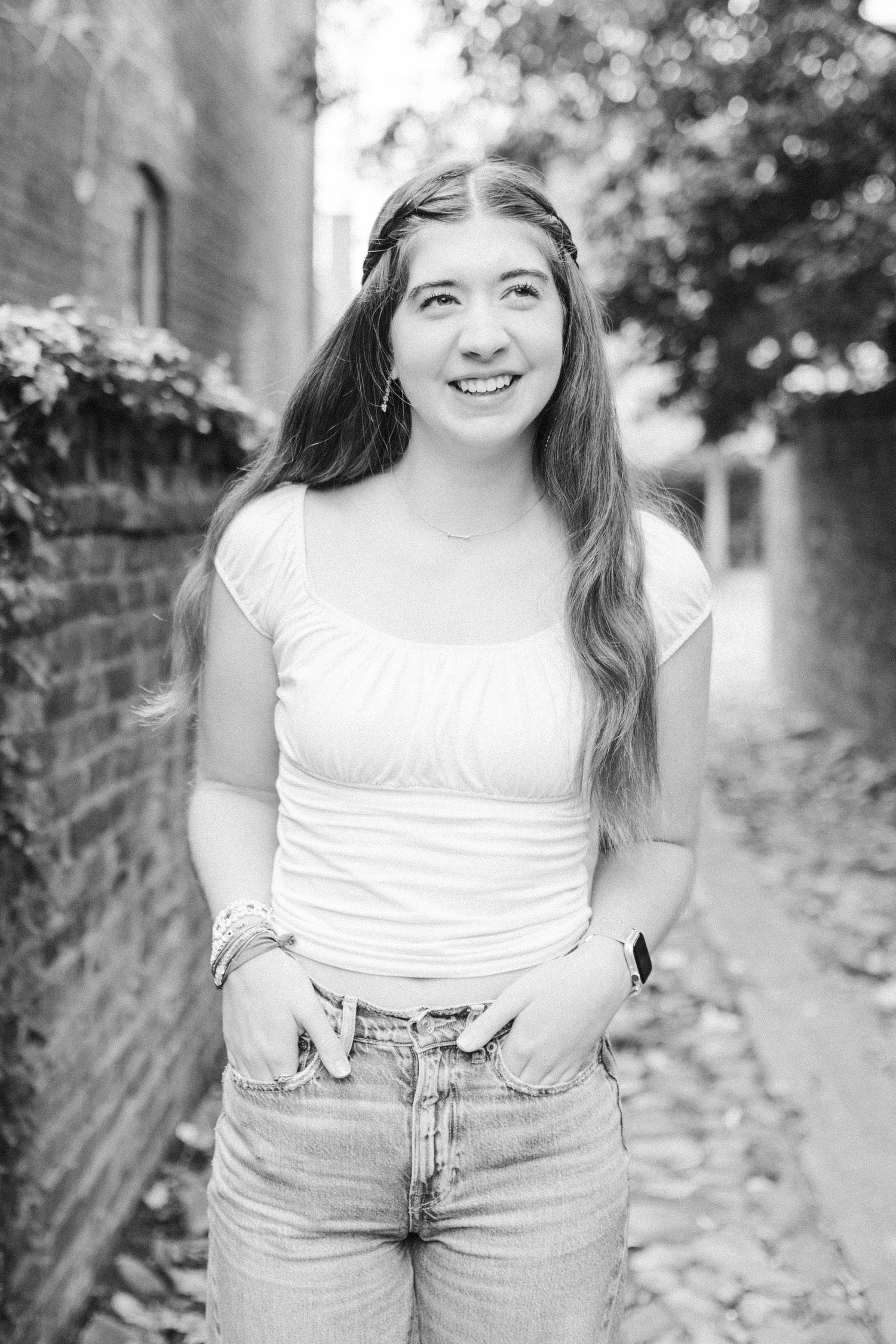 Black and white portrait of a person in a white top and jeans smiling outdoors.