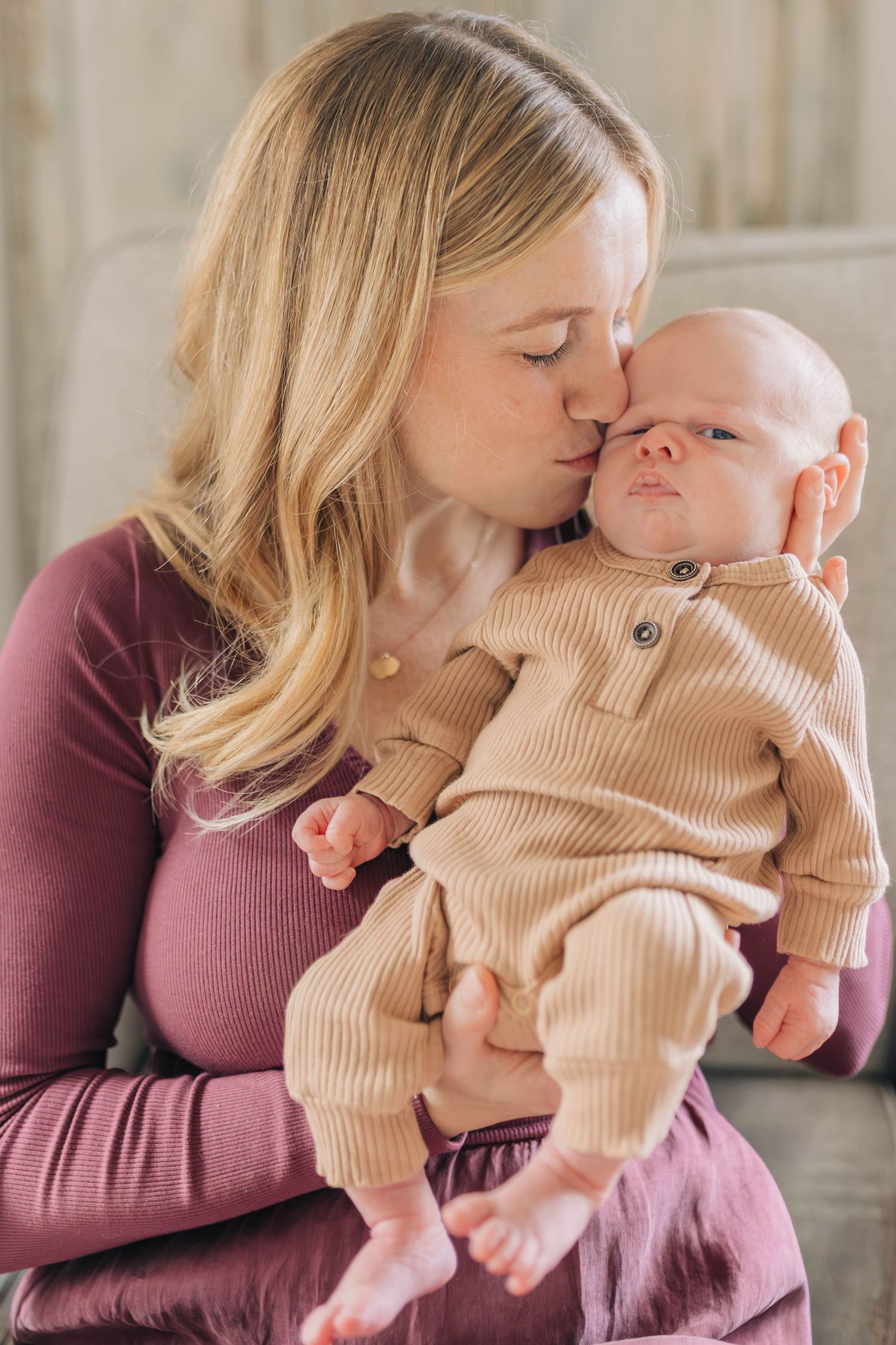 Intimate portrait of mother kissing baby in matching burgundy and beige outfits.