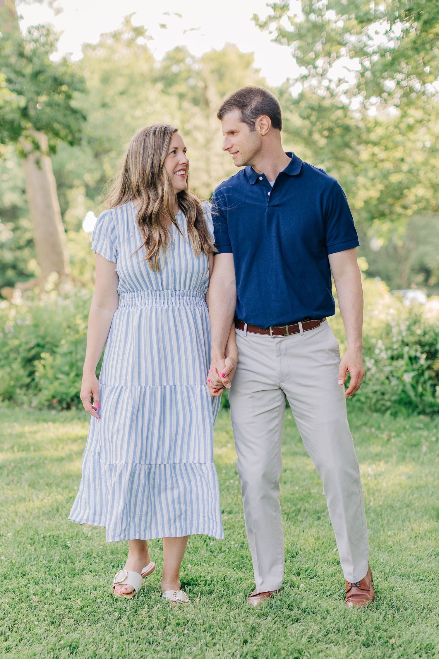 A couple in coordinated blue and white outfits walks together on grassy terrain.