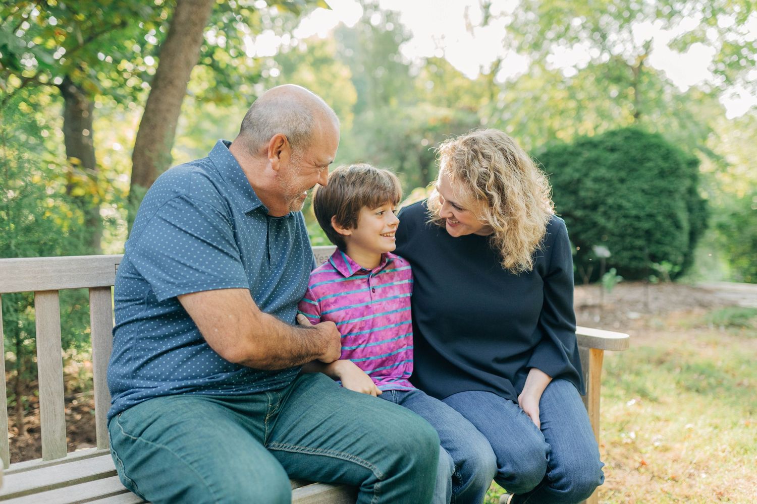 Family shares tender moments together on a wooden bench in a lush garden setting.