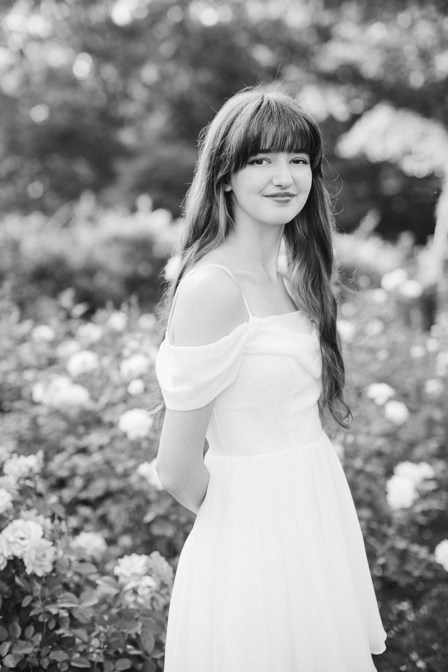 Classic black and white portrait of someone in an off-shoulder dress in a garden setting.
