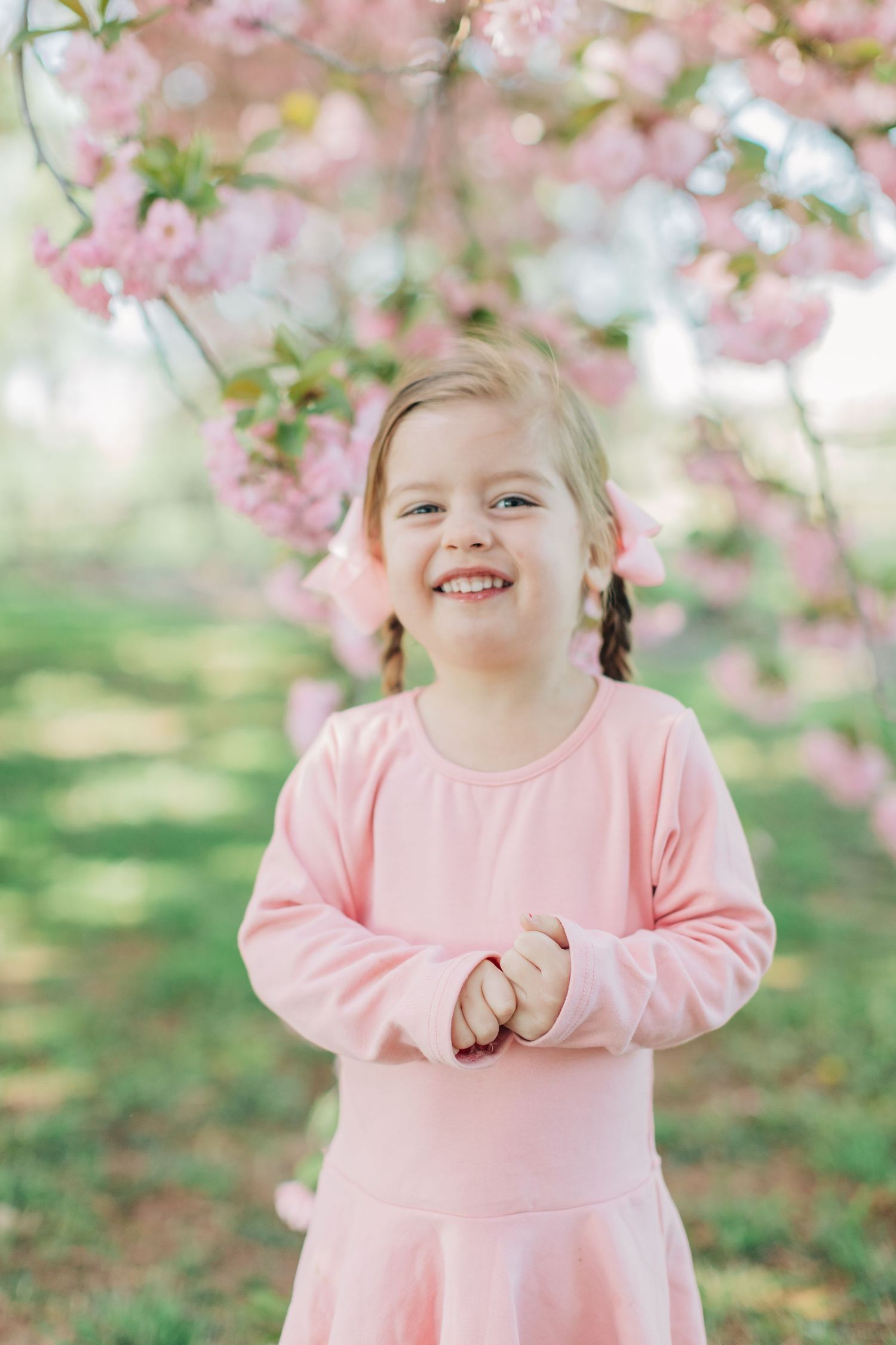 Happy child in pink dress laughing under spring cherry blossoms.