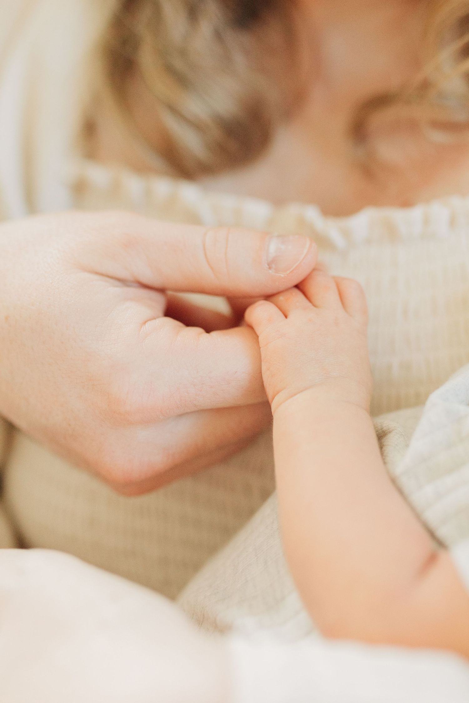 Close-up shot of tiny baby fingers grasping an adult hand against soft cream background.