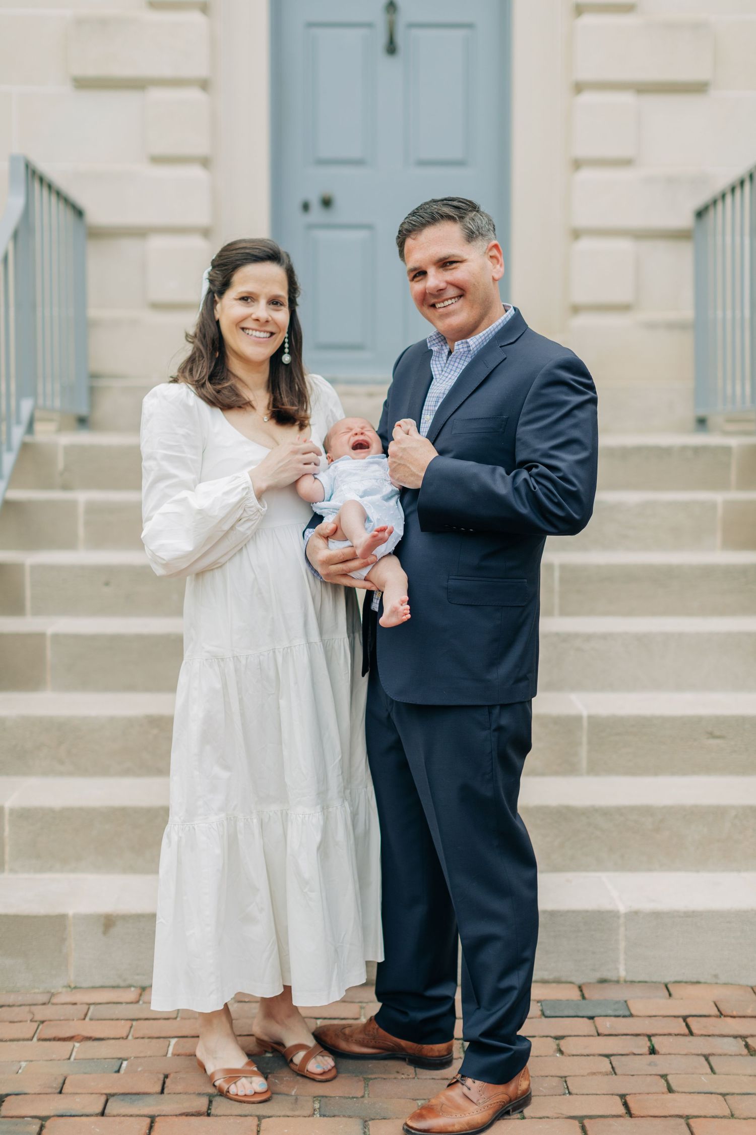 Family portrait session on brick steps featuring a white dress and navy suit with a newborn.