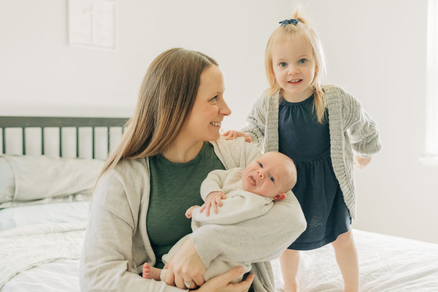 Happy family scene with toddler and infant sharing special bonding time on white bed.