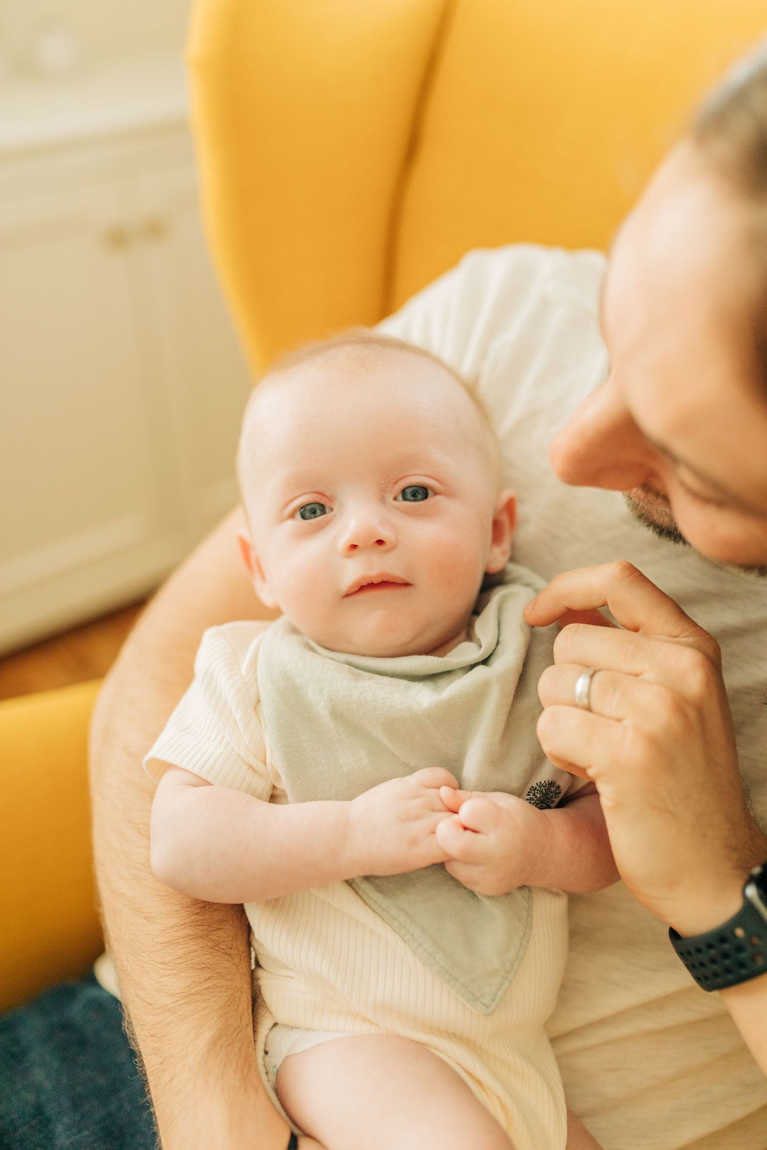 Close-up of gentle interaction on a yellow armchair in warm natural lighting.