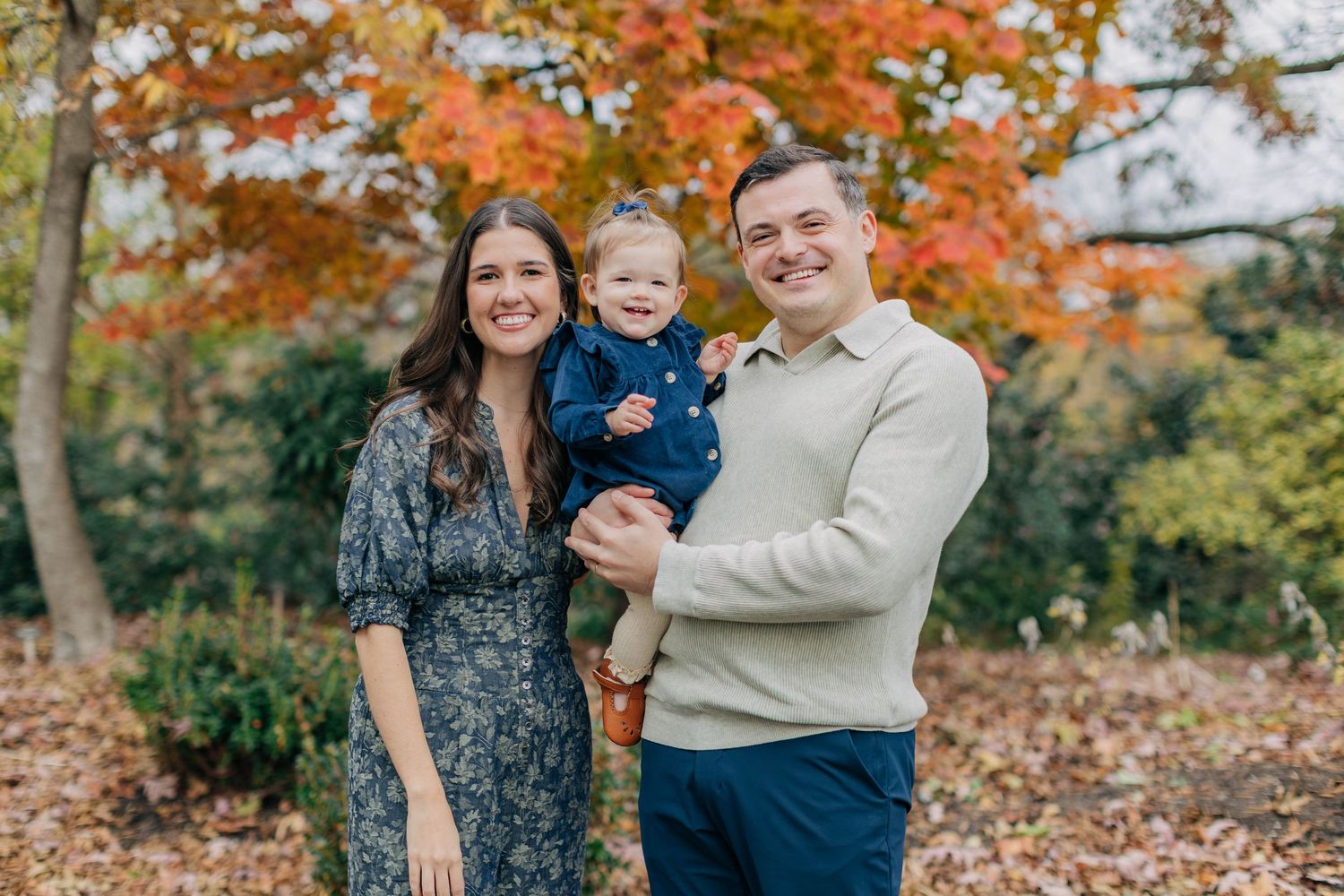 A candid family moment captured in a park with vibrant fall foliage in the background.