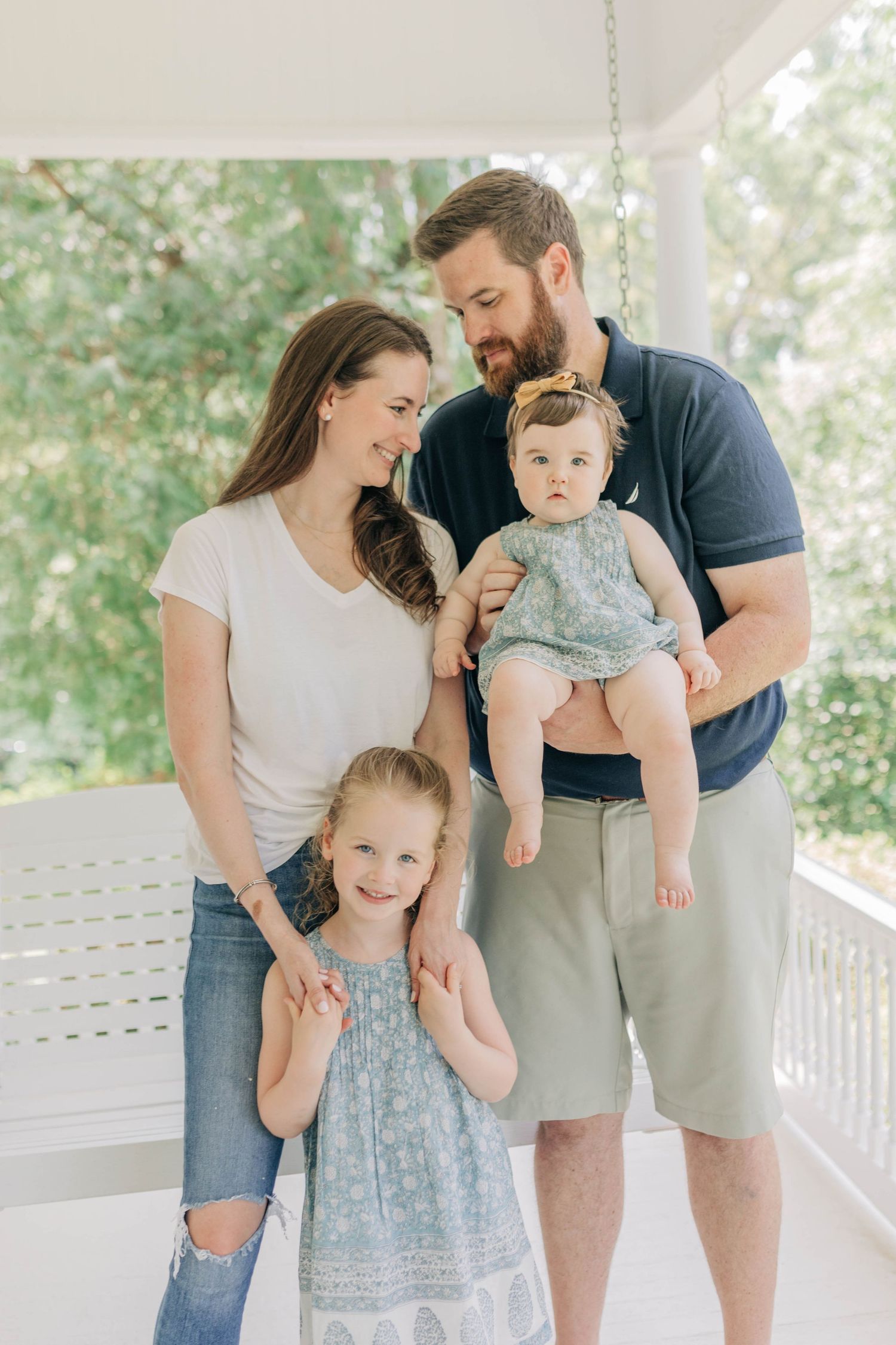 Family portrait moments on a white porch with natural greenery backdrop.
