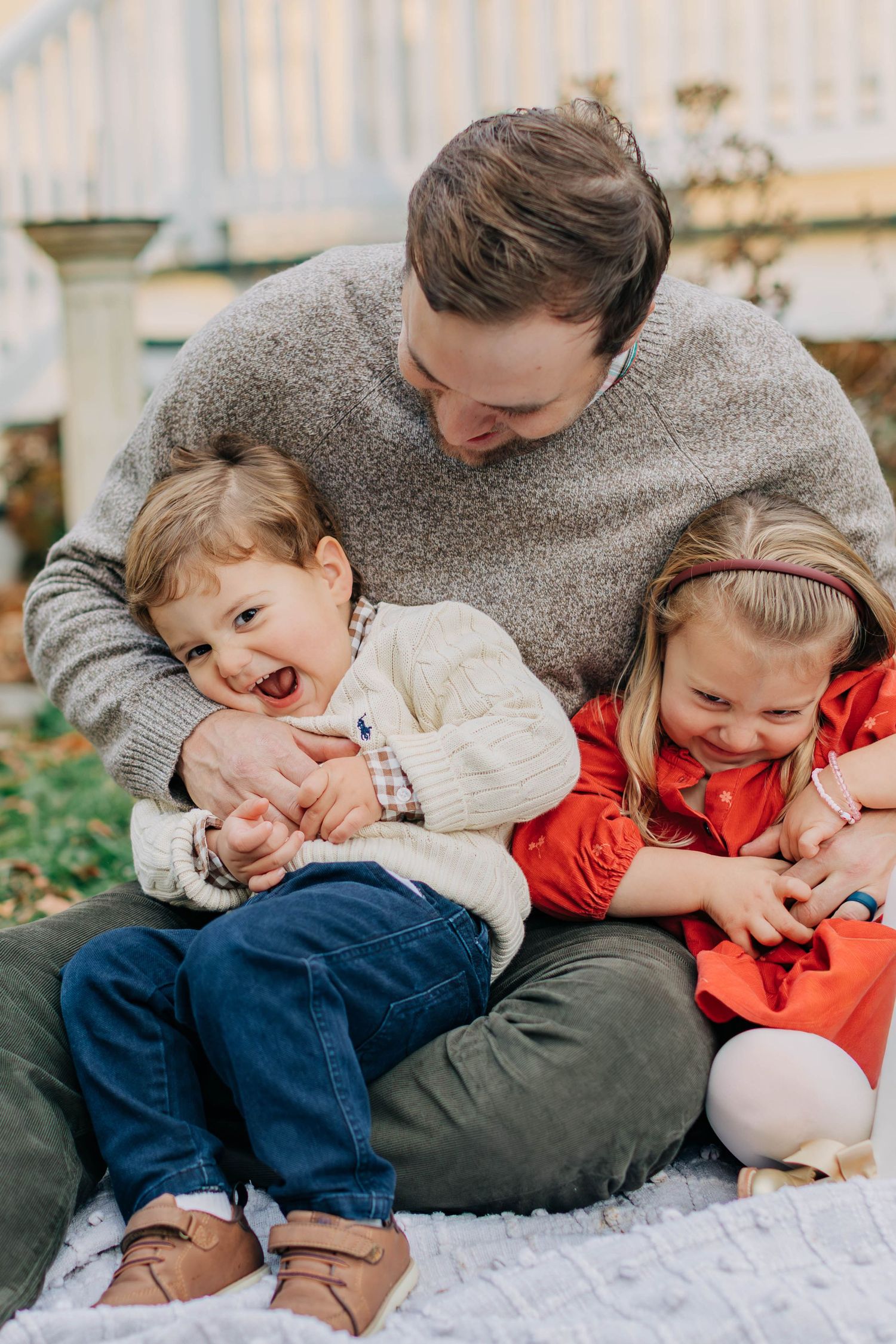 Candid family cuddle session captured on white blanket outdoors.