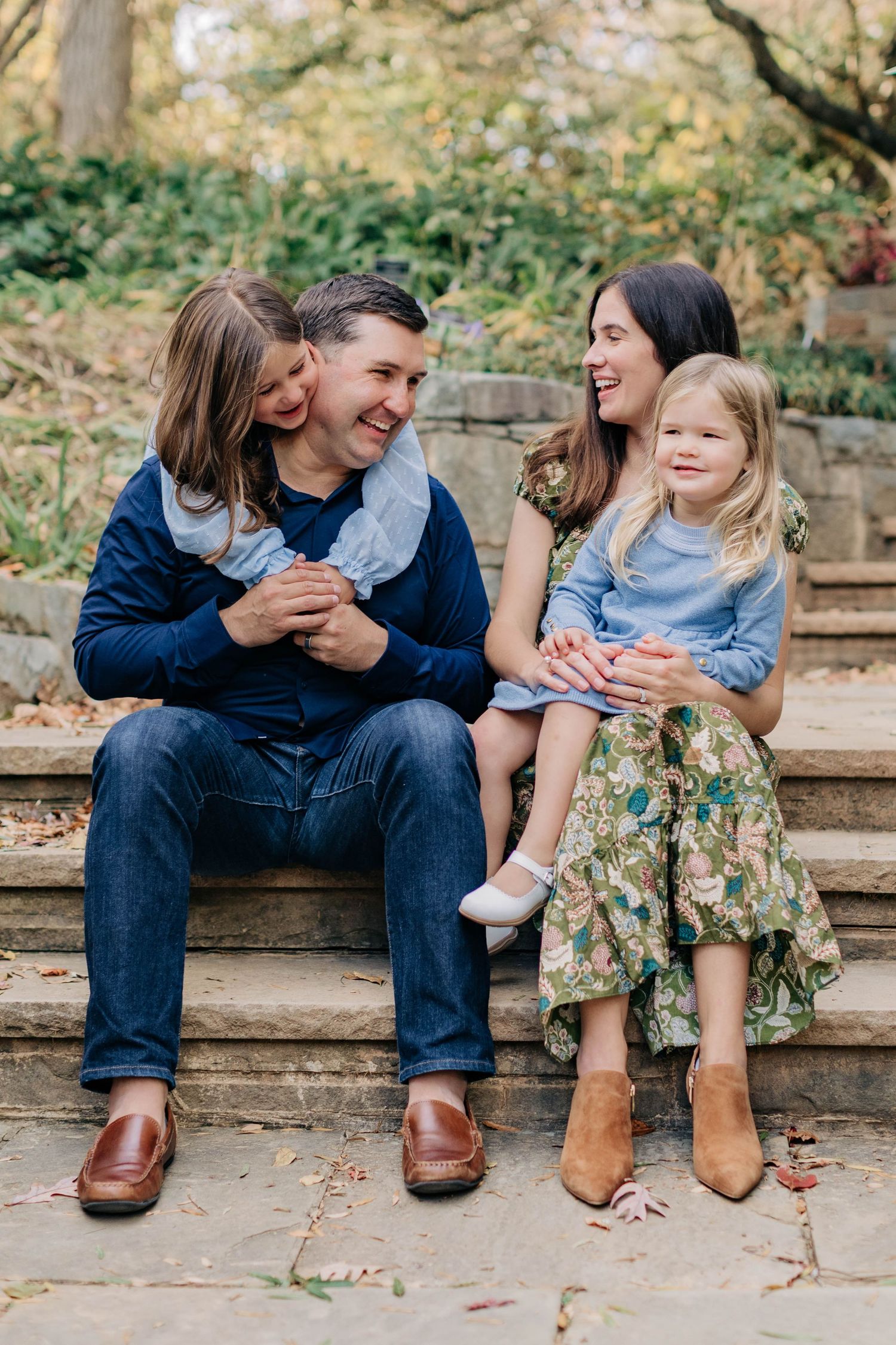 Family sits together on stone steps during autumn photo session wearing coordinating blue outfits.