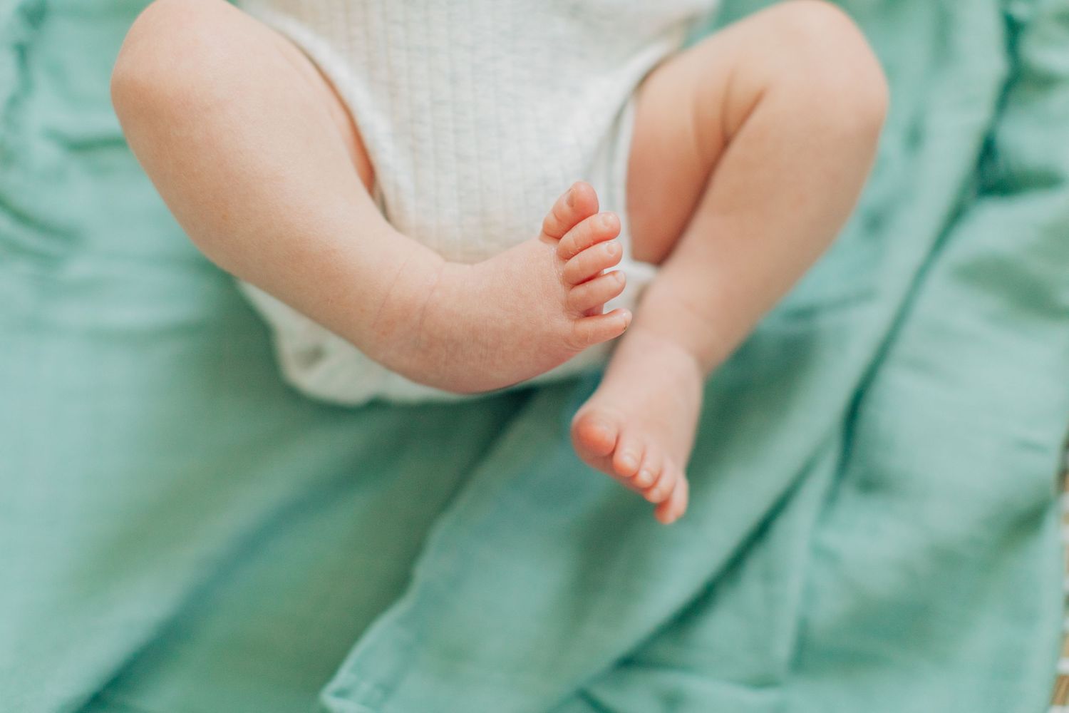 Tiny baby feet and legs resting on mint green blanket in soft lighting.