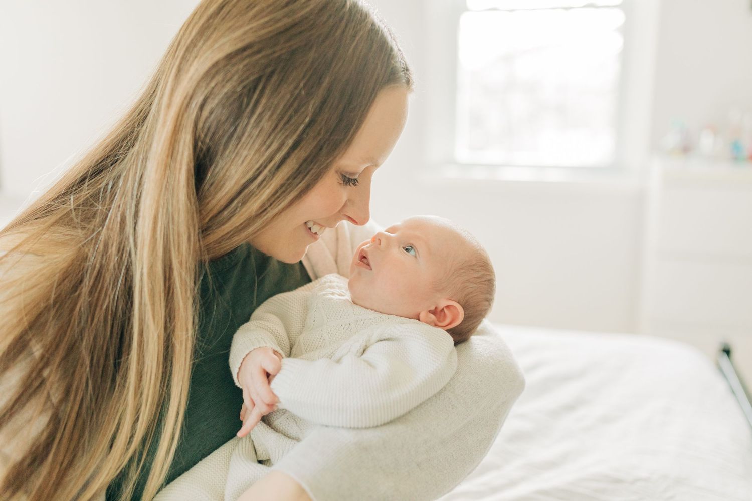Intimate close-up of tender moment with baby in cream colored outfit on white bed.