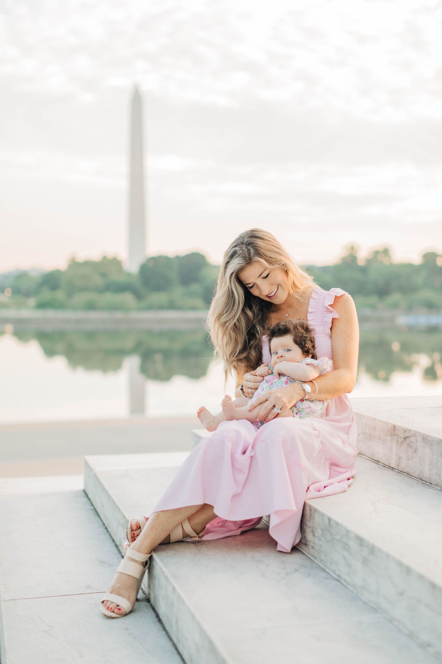 Woman in pink dress reclining on white stone steps during golden hour.