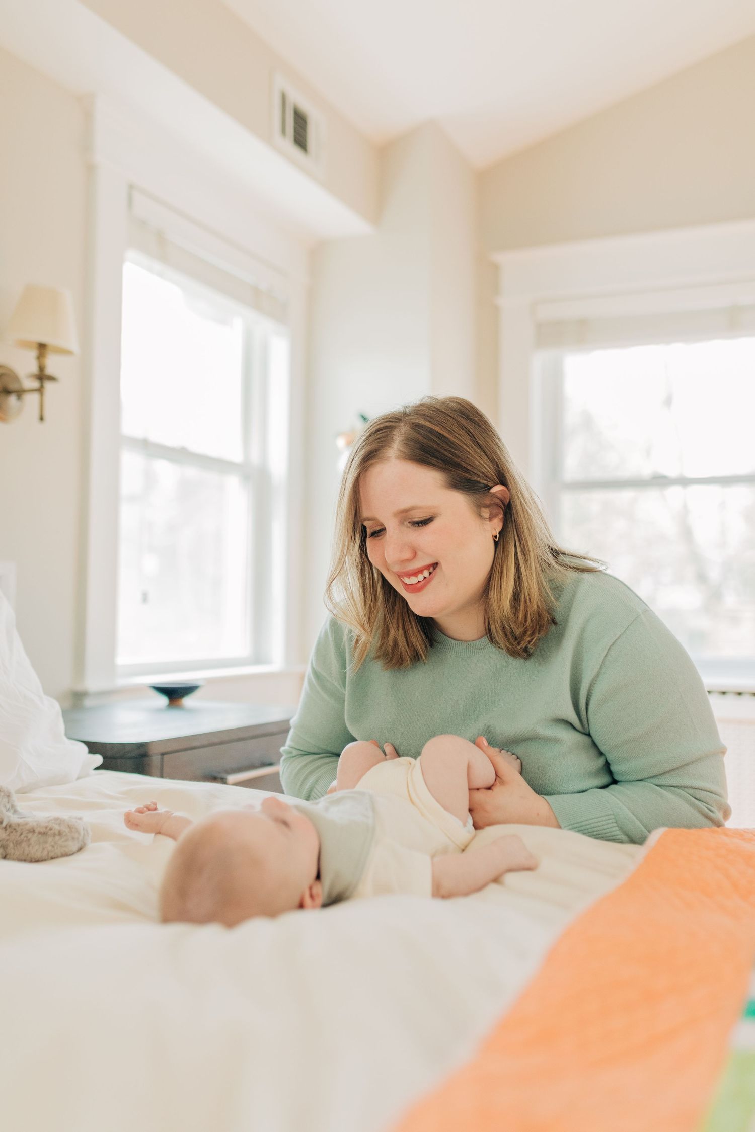 Parents in mint green sweater share tender moment with baby on white bedding in bright bedroom.