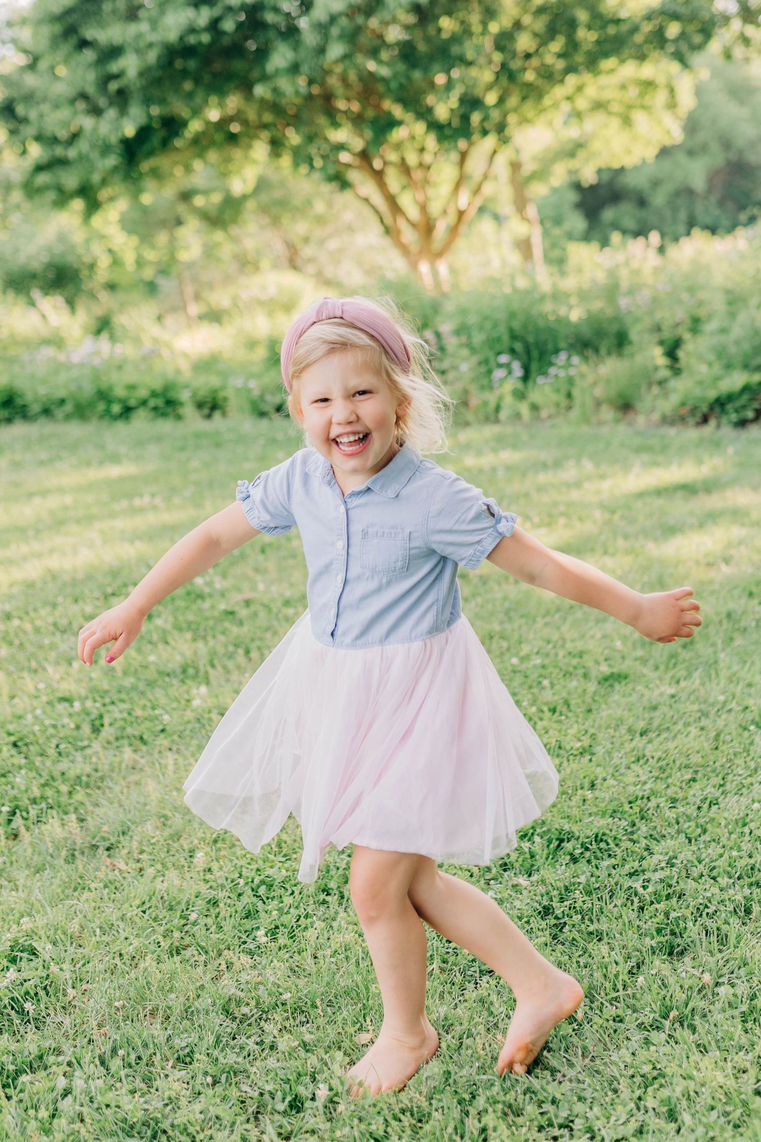 A child in a blue and white dress jumps playfully on green grass.