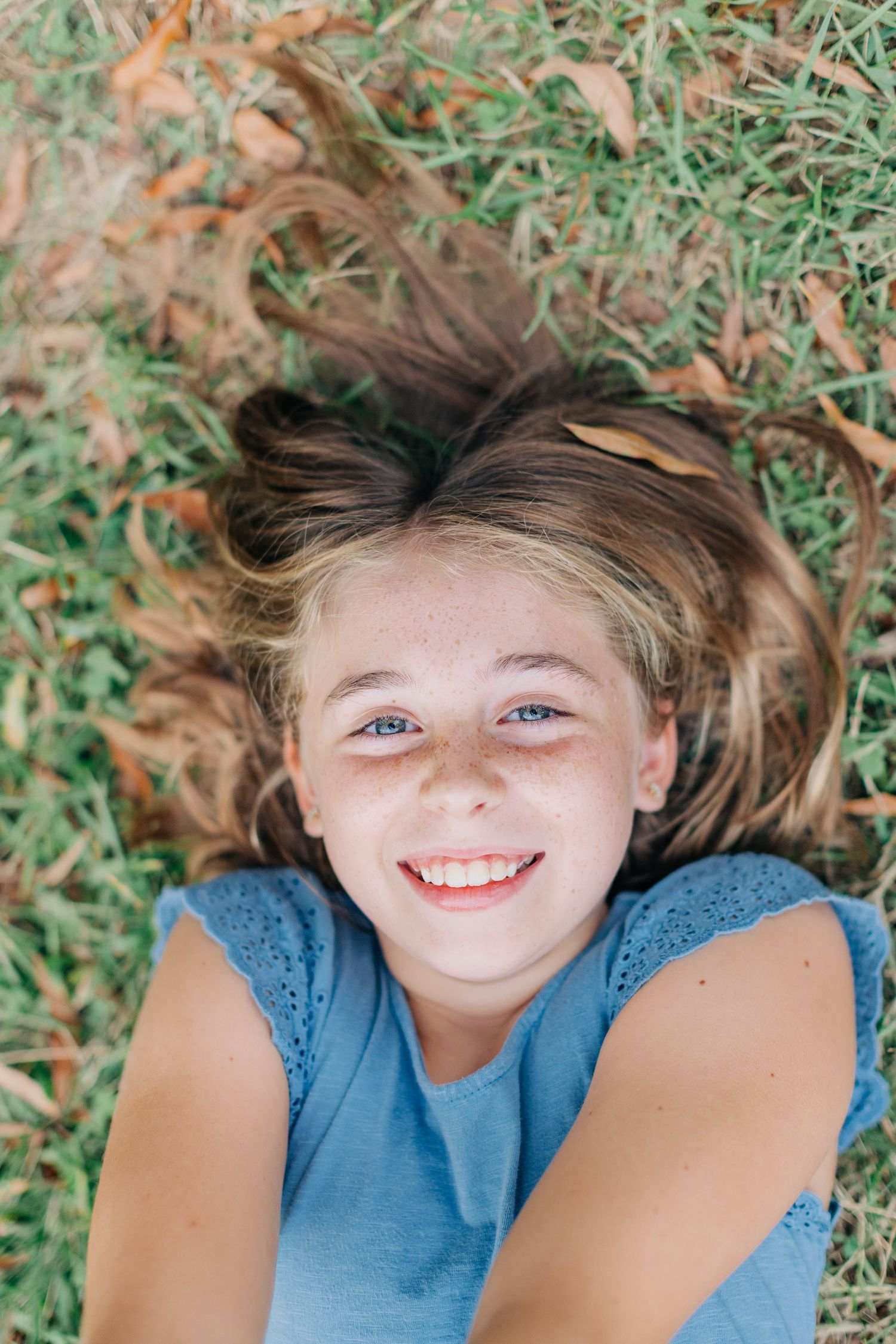 Close-up portrait of someone lying in grass with a bright, cheerful expression.