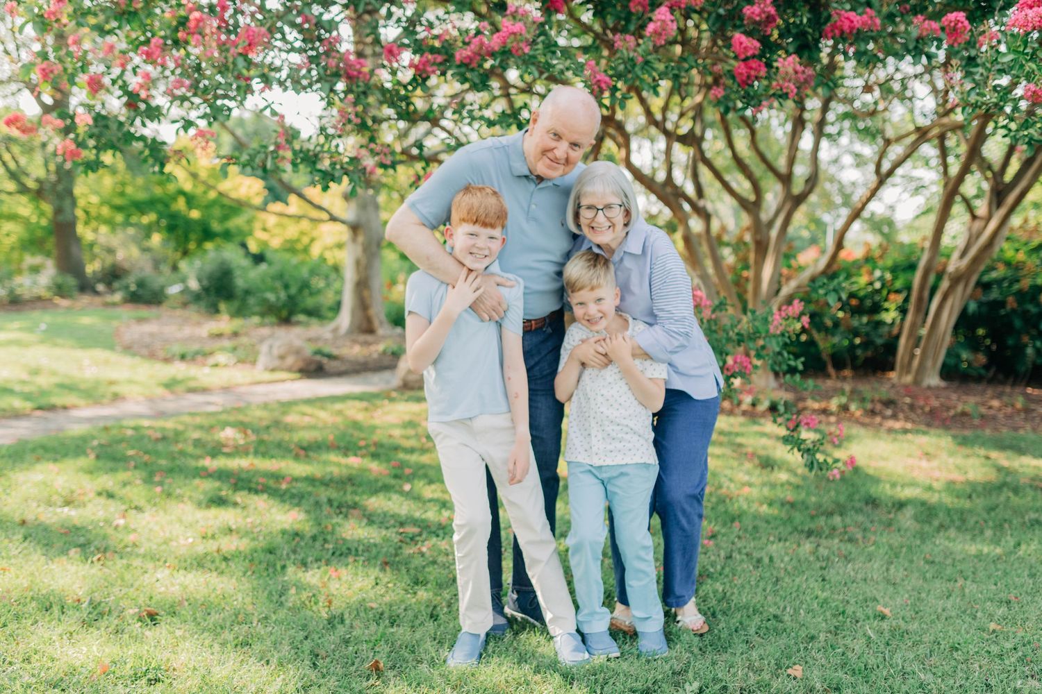 Candid family moment captured in a lush garden setting with pink flowering bushes.