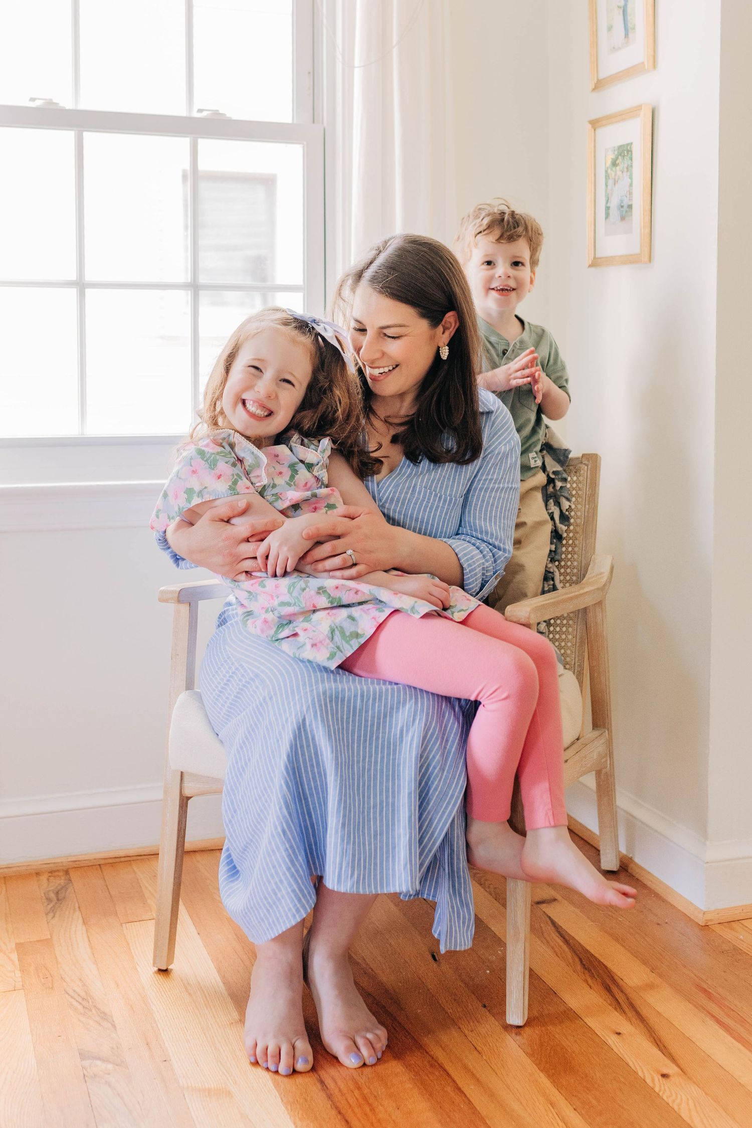 Family sharing a tender moment while sitting in a wooden chair by the window.