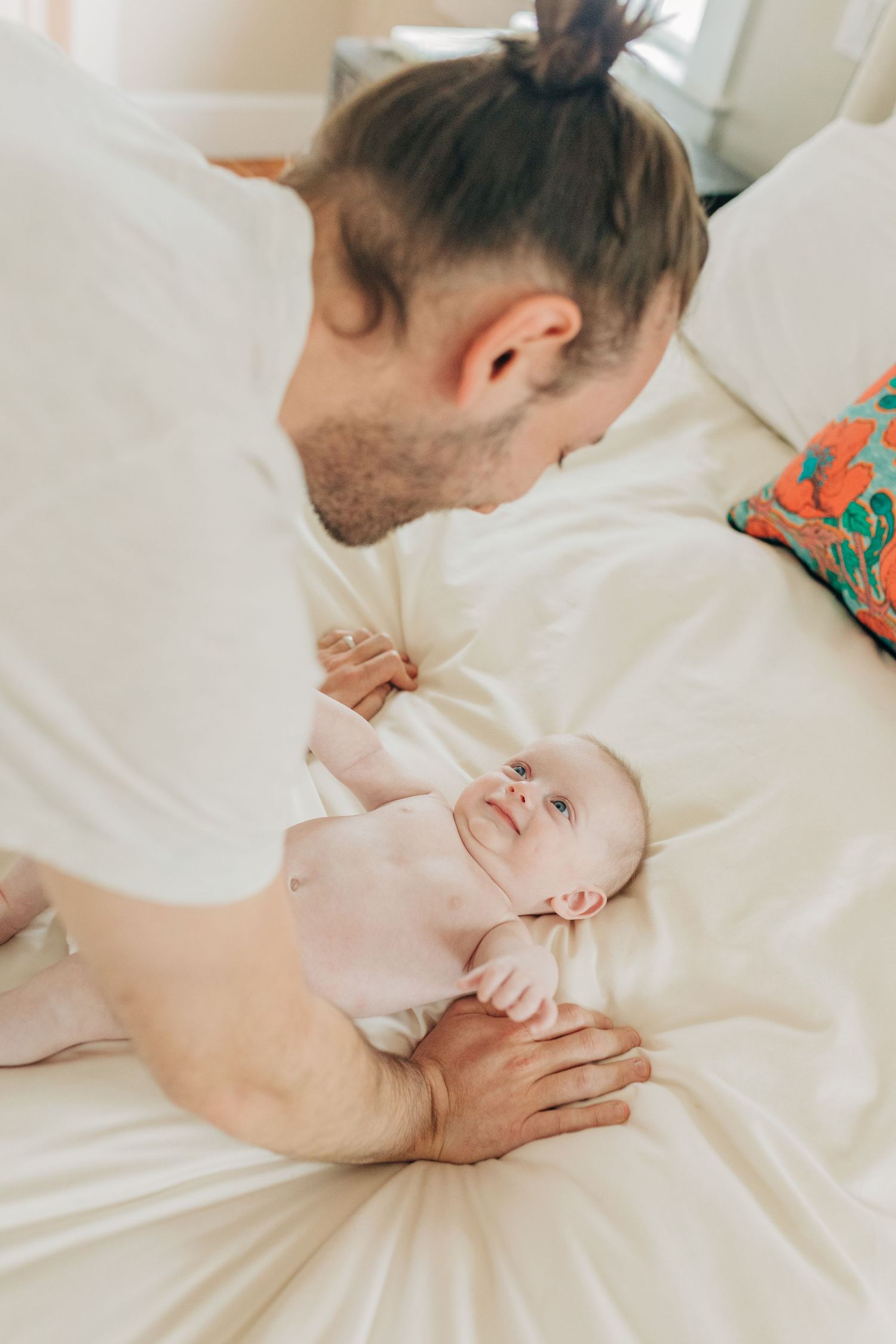 A tender moment between parent and infant lying on white bedding.