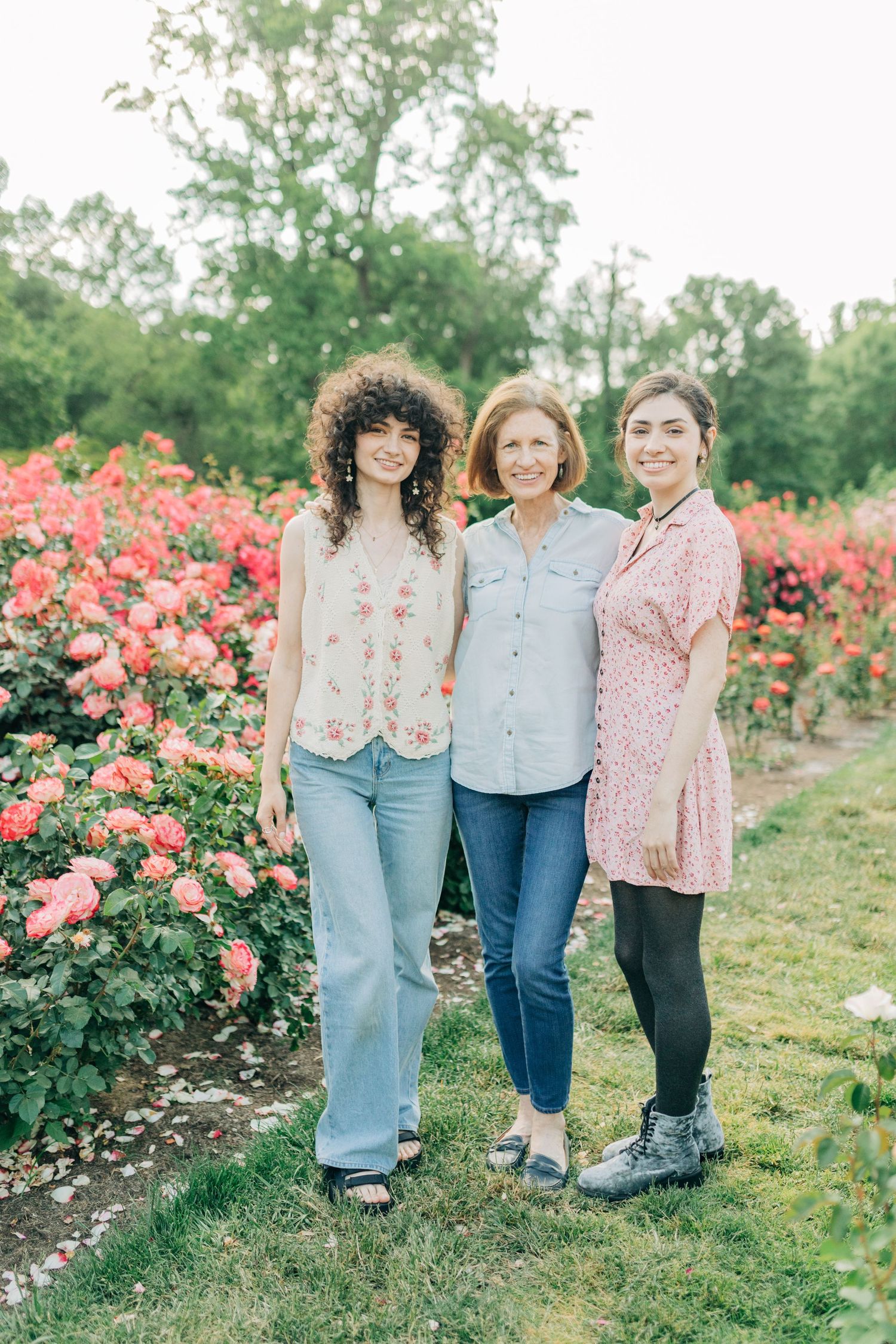 Three people stand together smiling in a beautiful rose garden with pink blooms.
