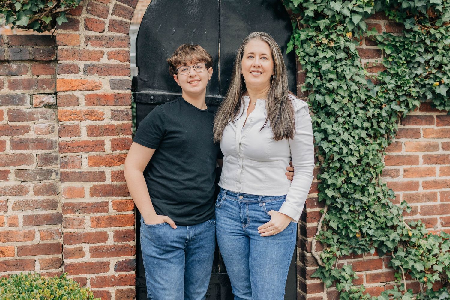 Two people in casual outfits posing against a brick wall with climbing ivy.