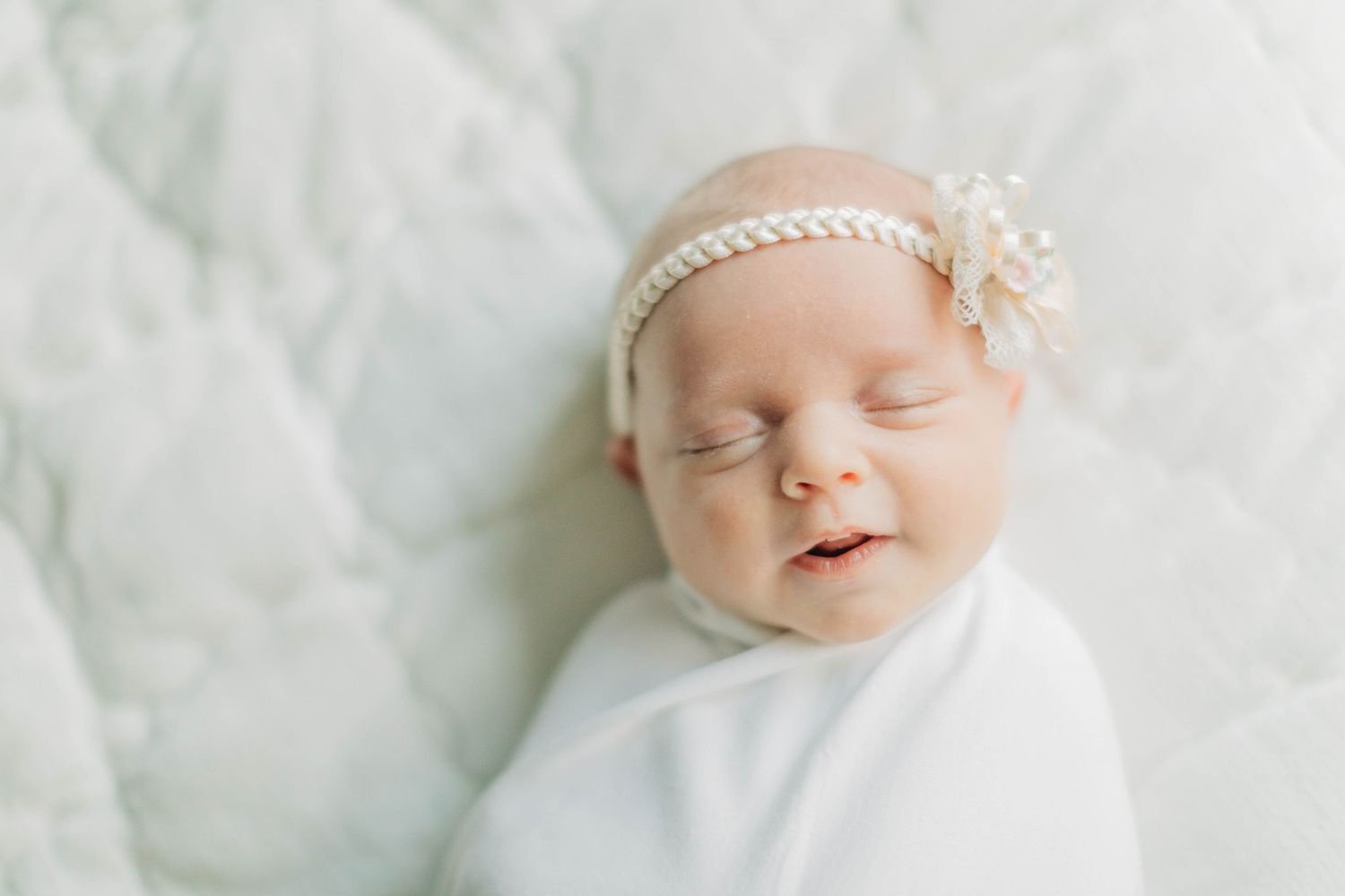 Close-up portraits of sleeping newborn baby in white against soft textured background.