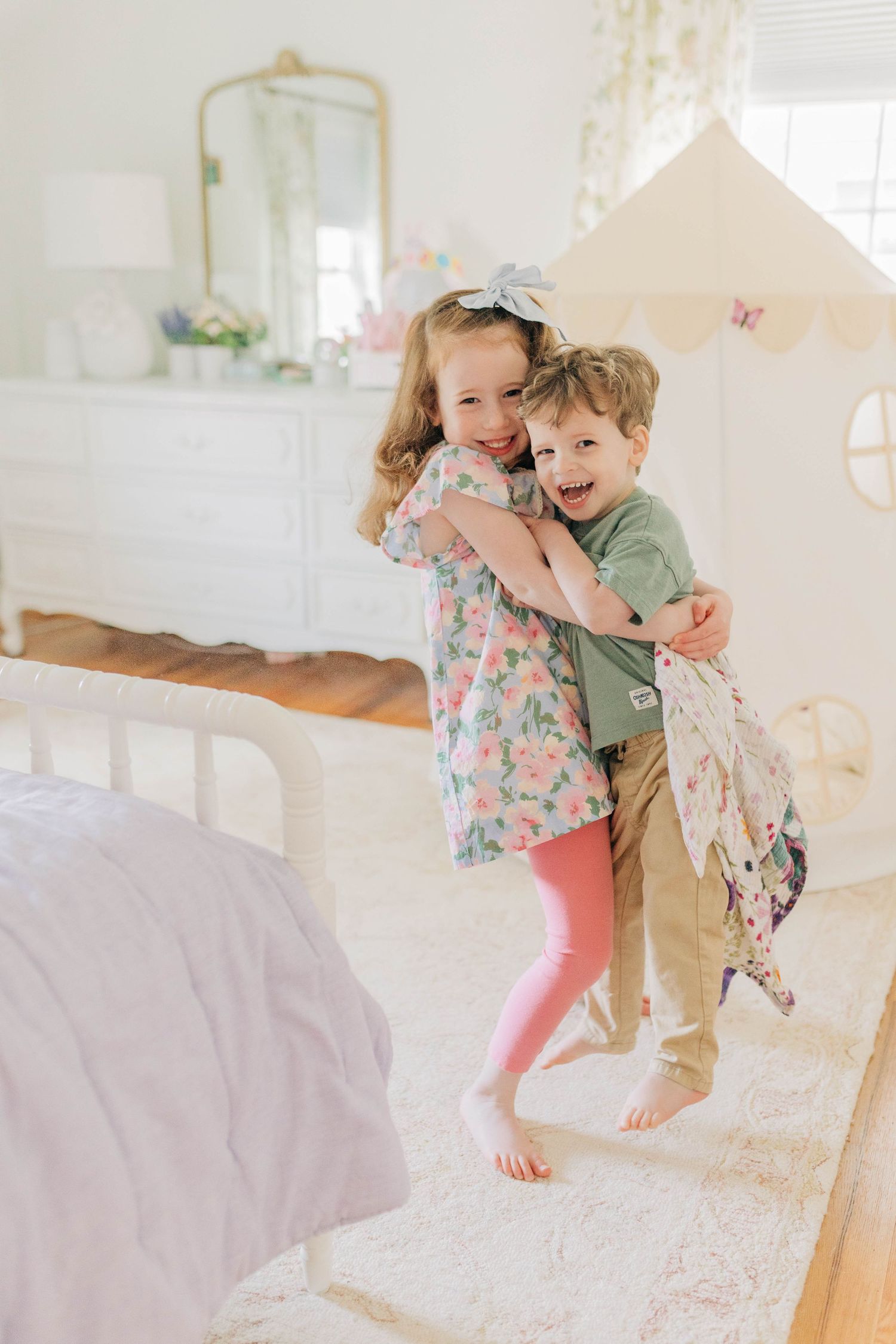 Two children in casual clothes playing and jumping together on a white bed.