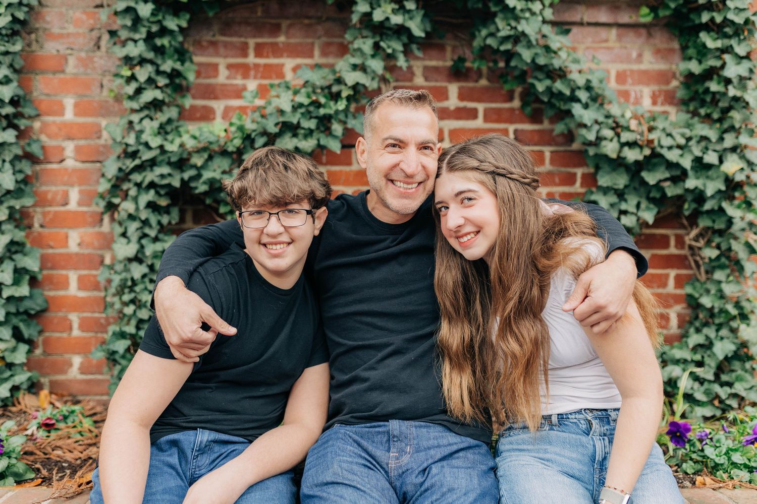 Three people sitting together and laughing against an ivy-covered brick wall backdrop.