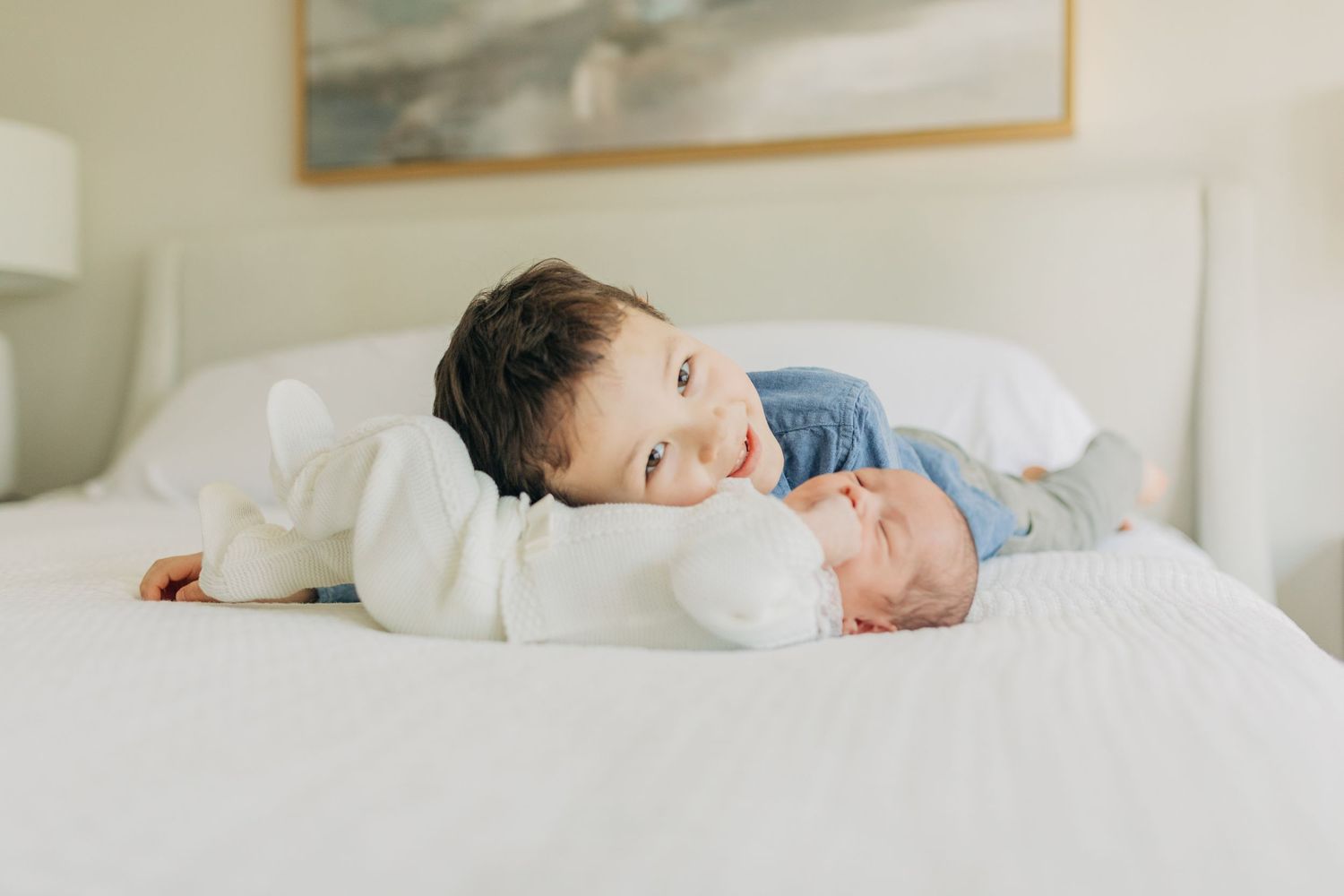 Two children interact sweetly on a white bed in a bright bedroom.