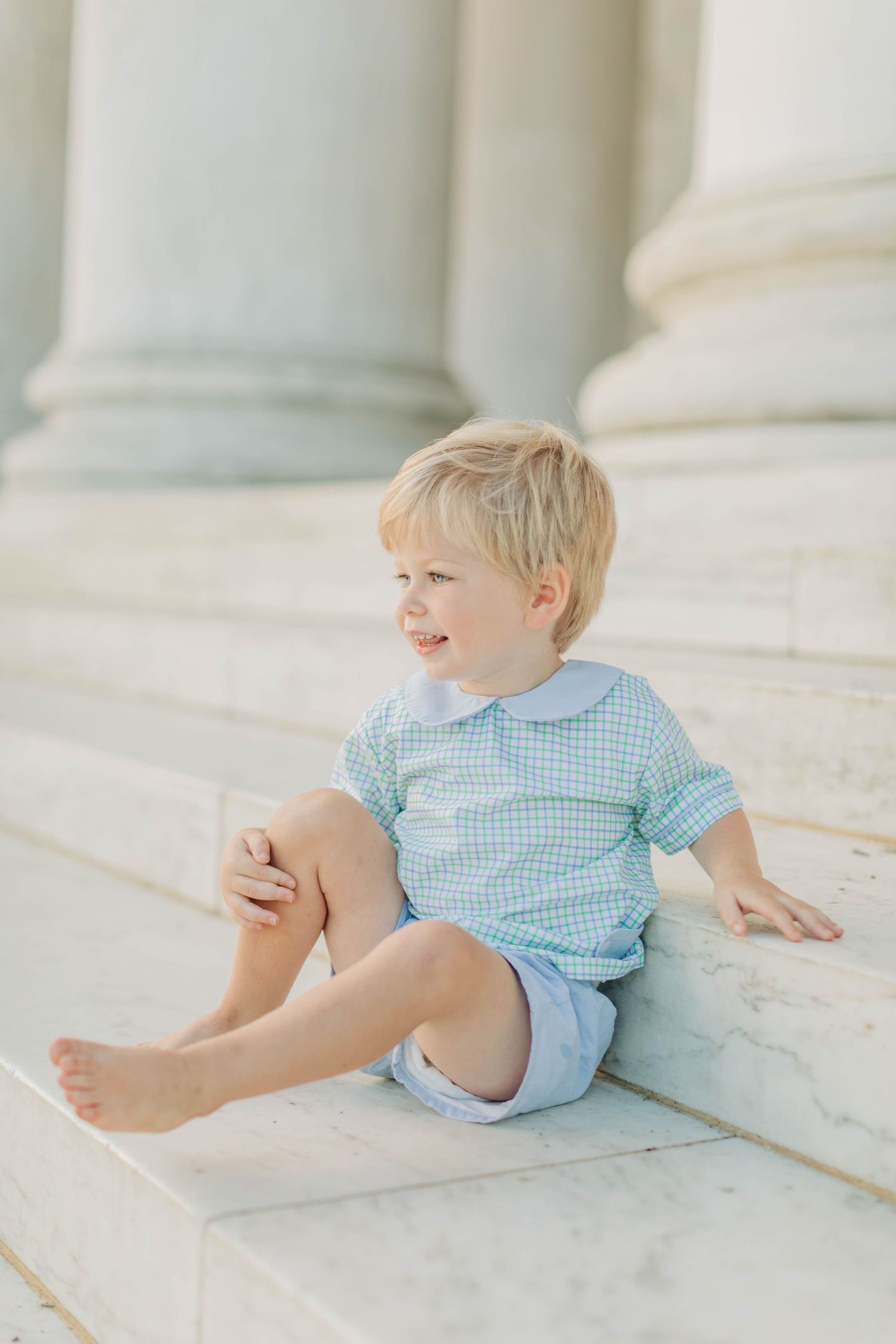 Young child in blue gingham sitting on white marble steps of a monument.