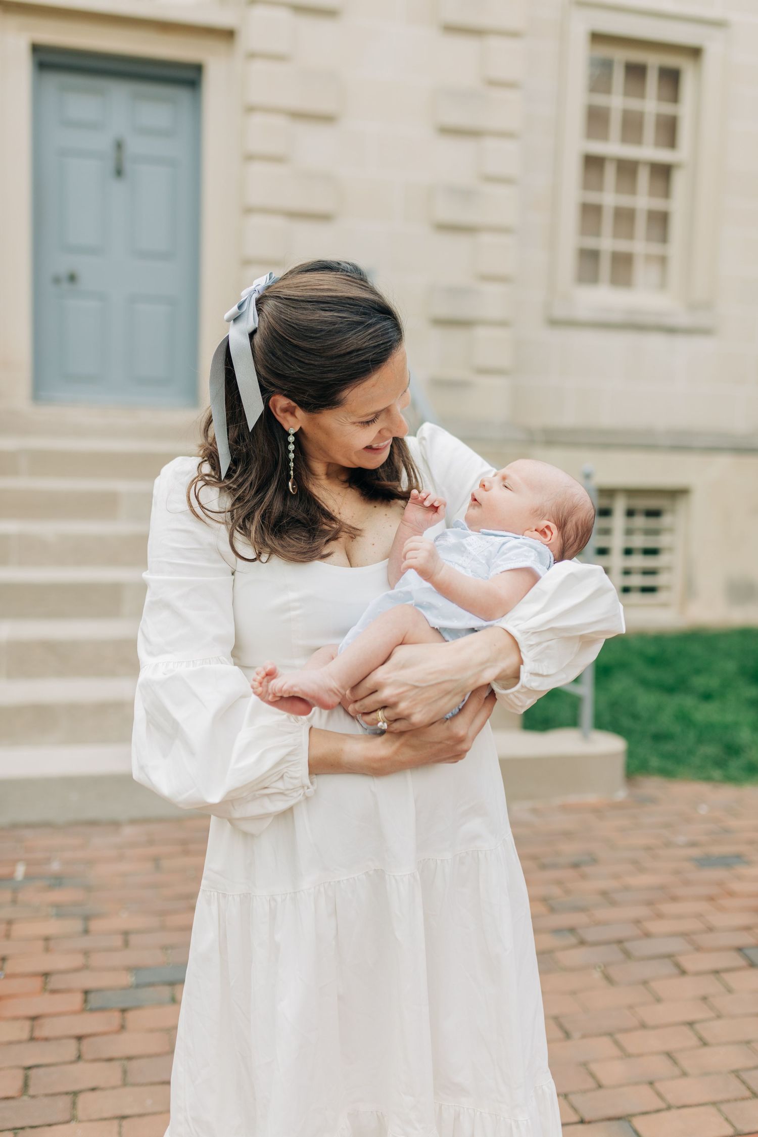 Tender interaction between parent and baby in front of a classic colonial building.