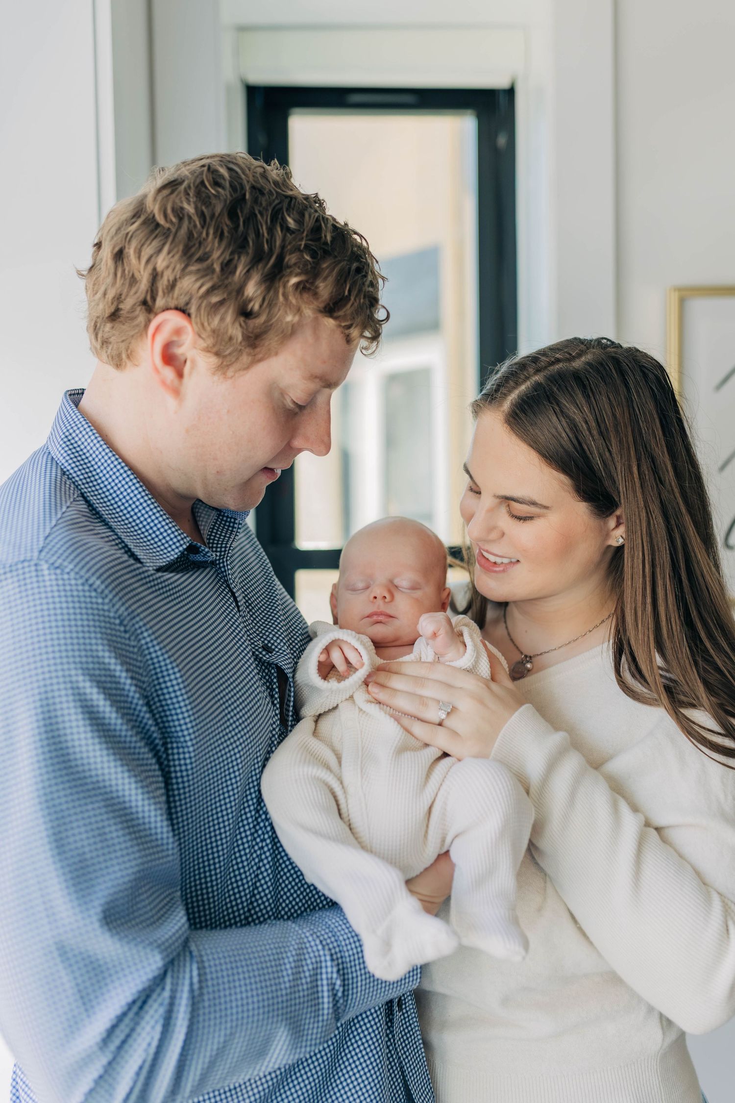 New parents tenderly gazing at their sleeping newborn baby dressed in white.