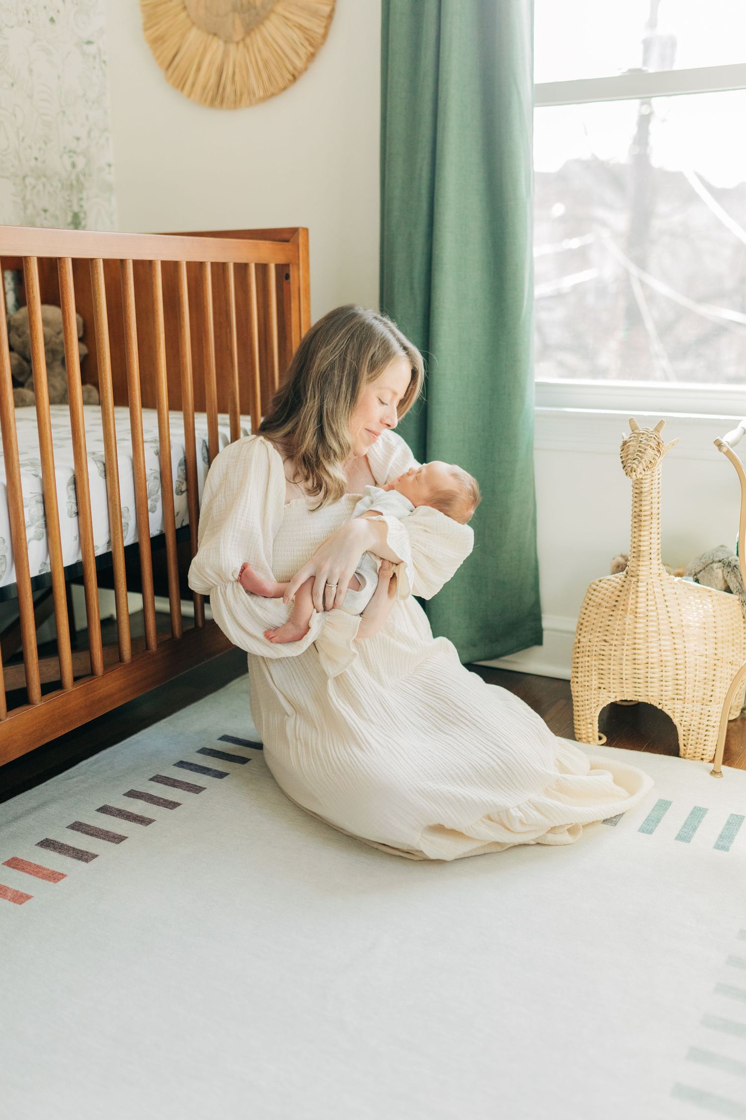 Serene nursery scene with mother and baby near wooden crib and green curtains.