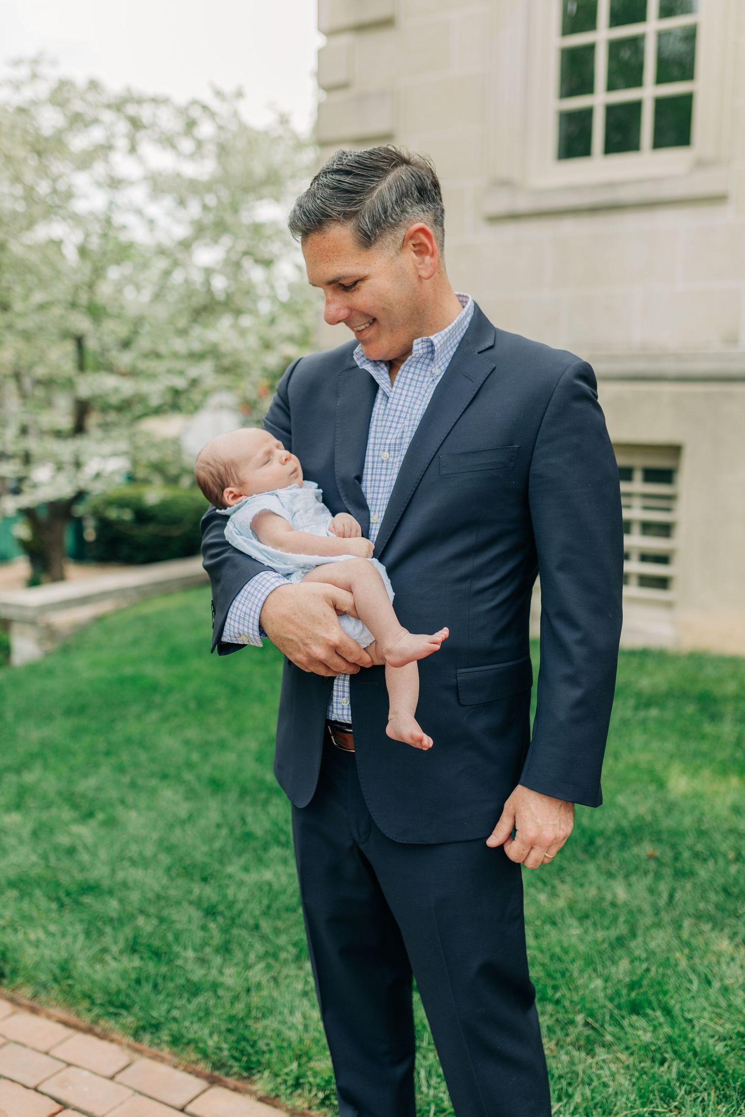 Sweet interaction between a suited figure and infant on a sunny day near a building.