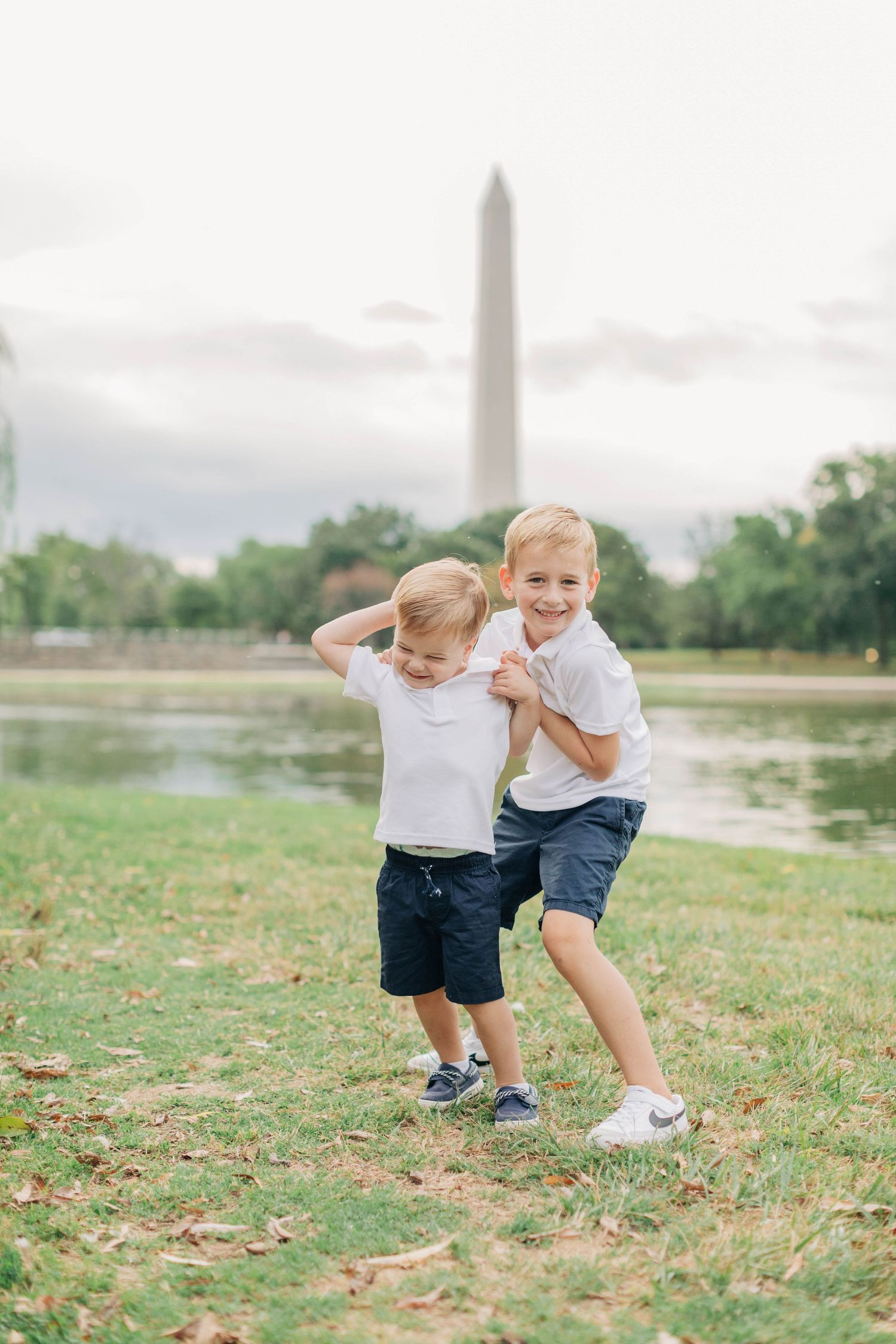 Two children play on grassy grounds near the Washington Monument on an overcast day.