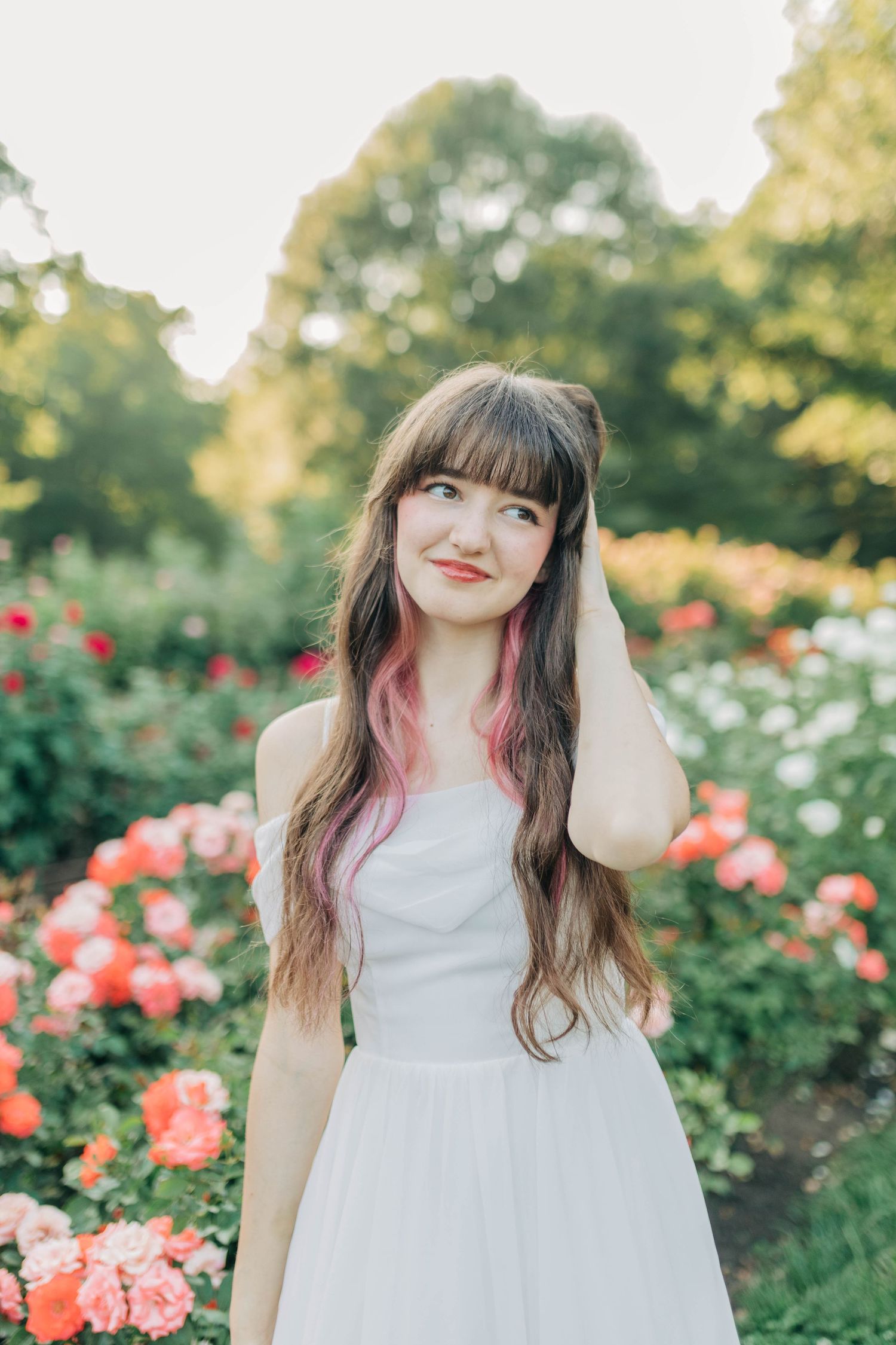 Candid garden portrait with someone in white dress surrounded by coral roses.