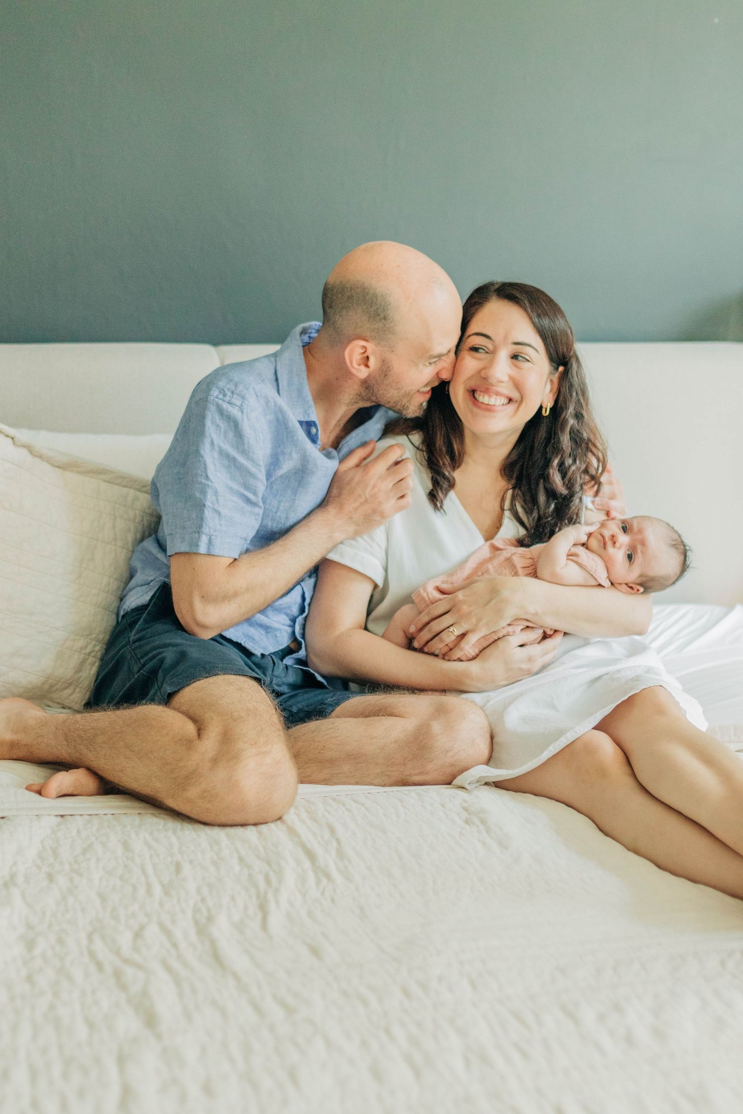 Intimate lifestyle photos of family cuddling together on white bed.