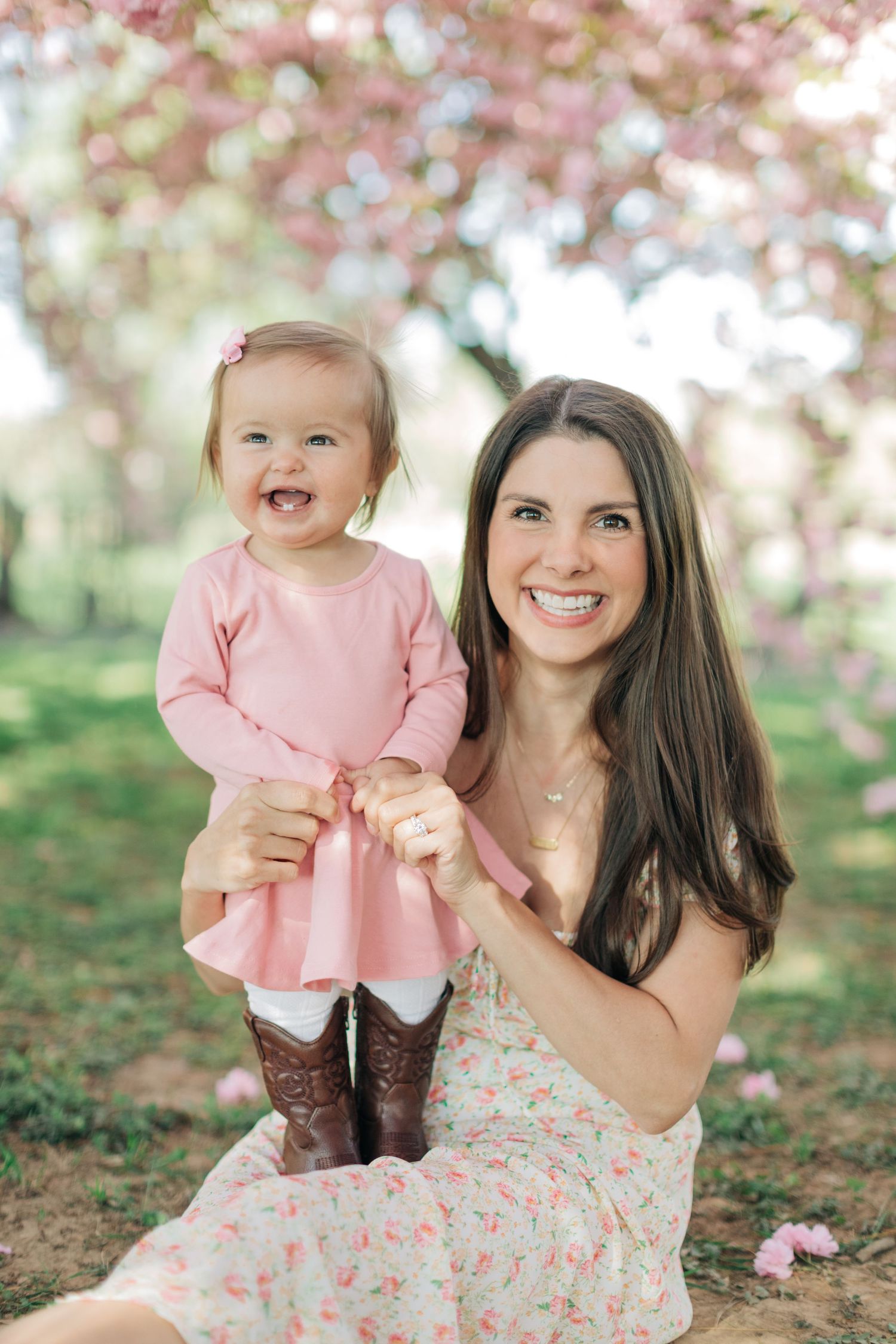 A sweet moment captured under pink cherry blossoms wearing coordinating floral and pink dresses.