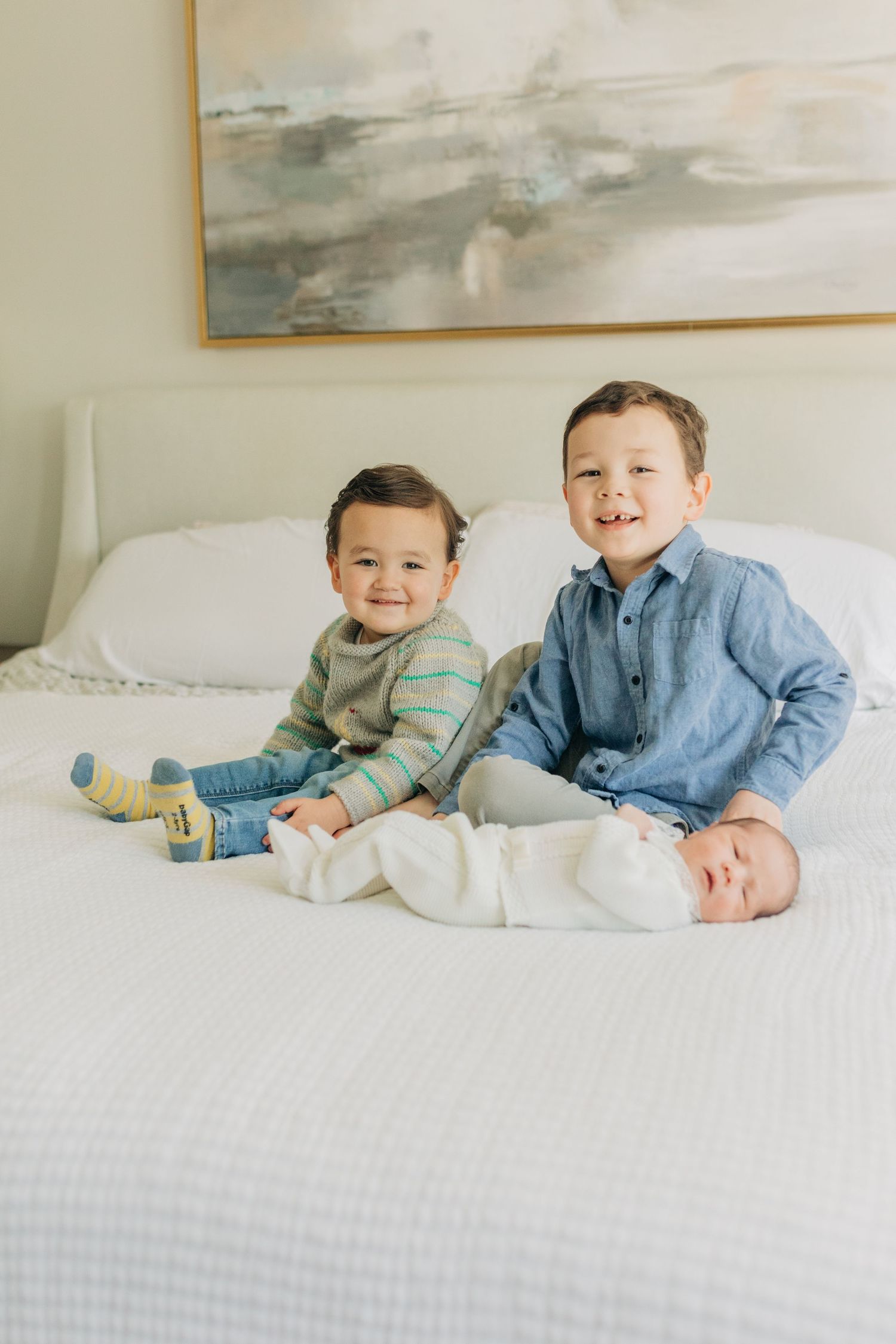 Children lounging on a bright white bed with a modern art piece on the wall.